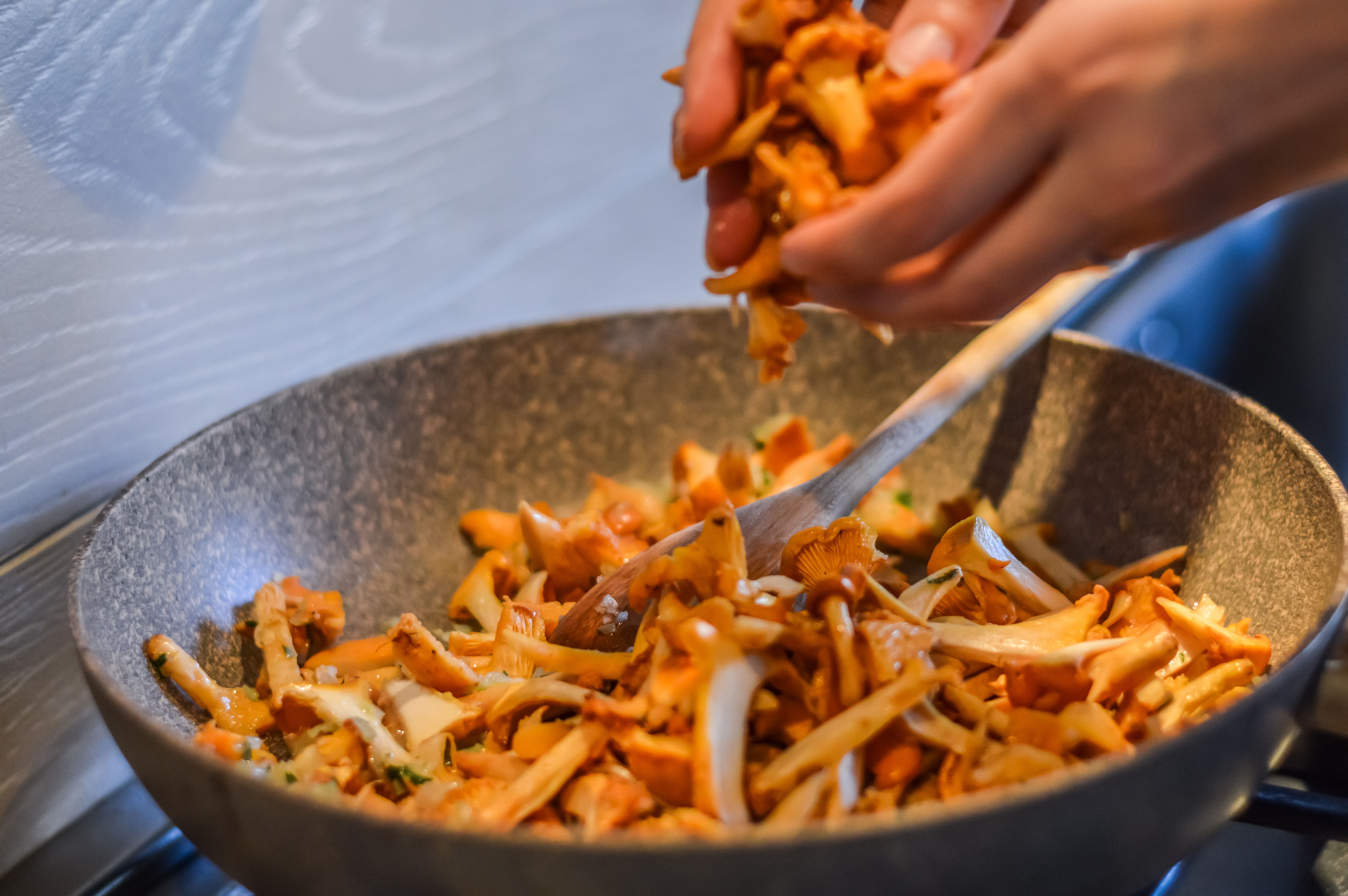 Pfifferlinge werden in eine Pfanne mit bereits bratenden Pilzen gegeben.