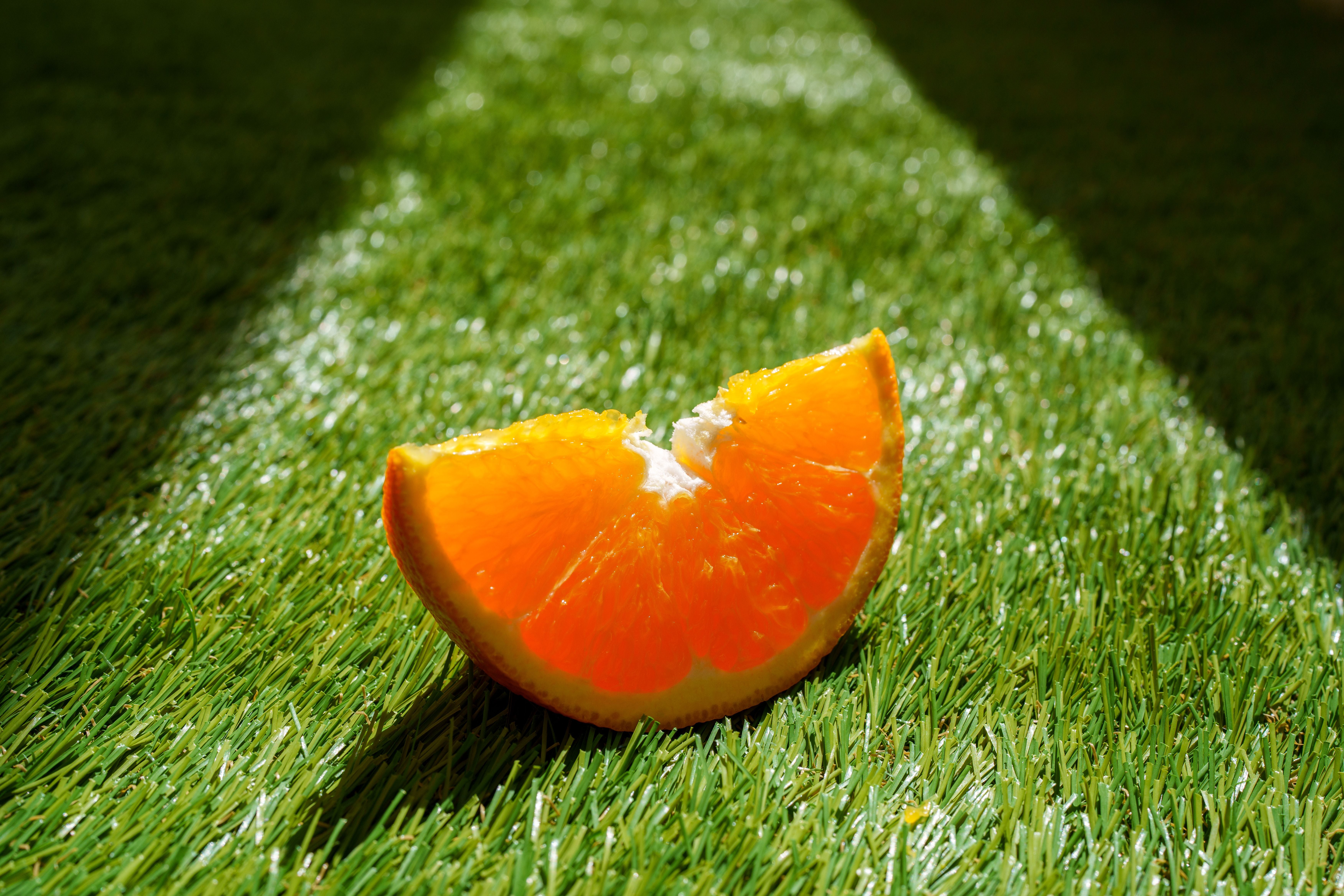 Orangenschnitz auf grünem Kunstrasen im Sonnenlicht.