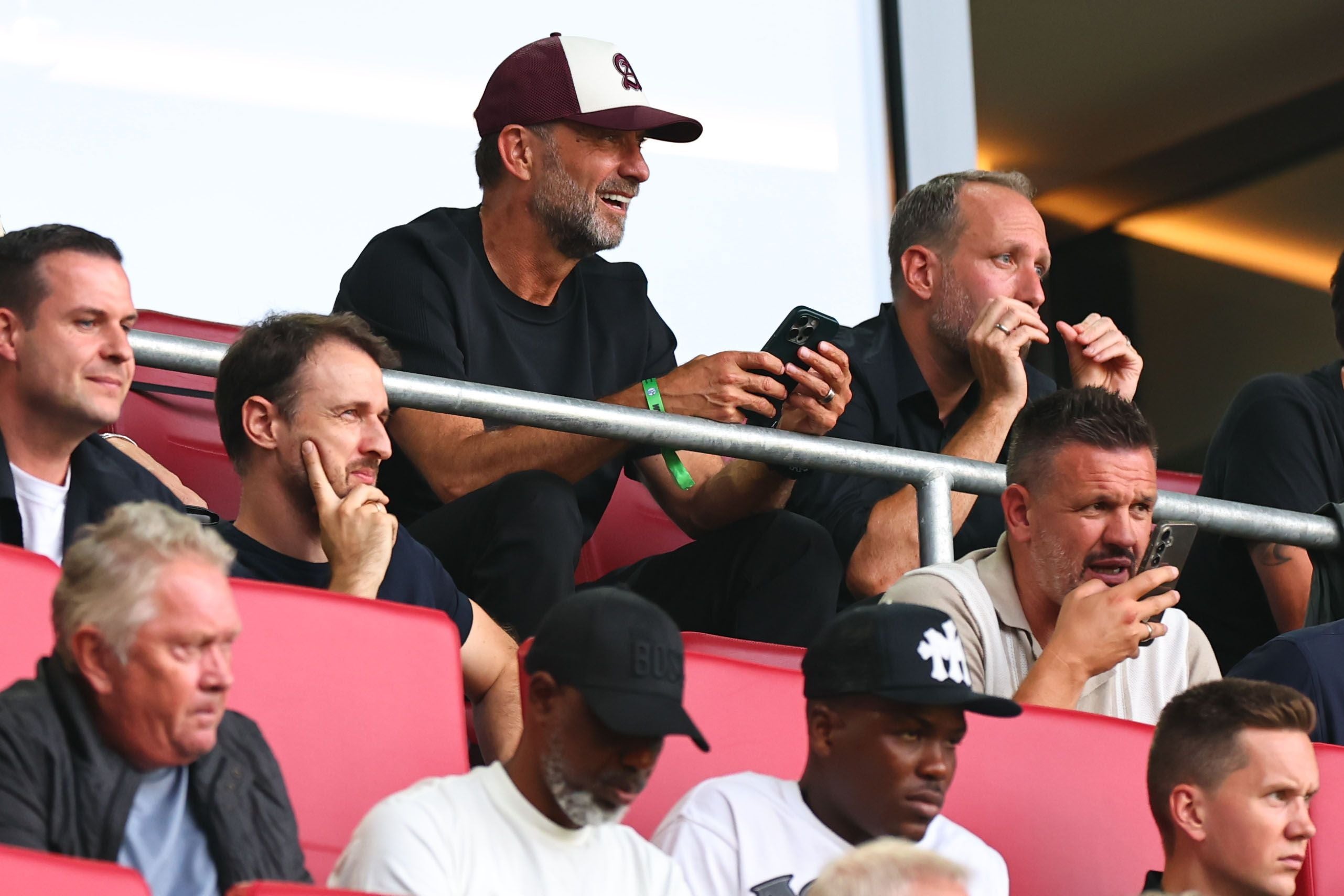 Mehrere Männer sitzen auf Stadiontribünen und beobachten ein Fußballspiel.