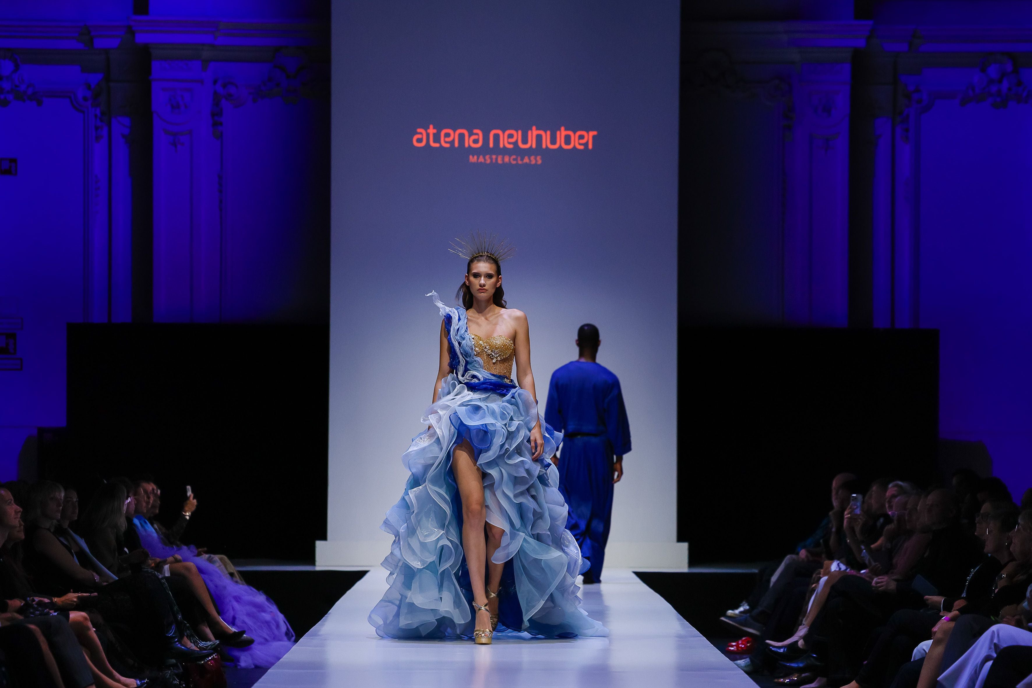 Model auf dem Laufsteg in einem blauen, voluminösen Kleid bei einer Modenschau.