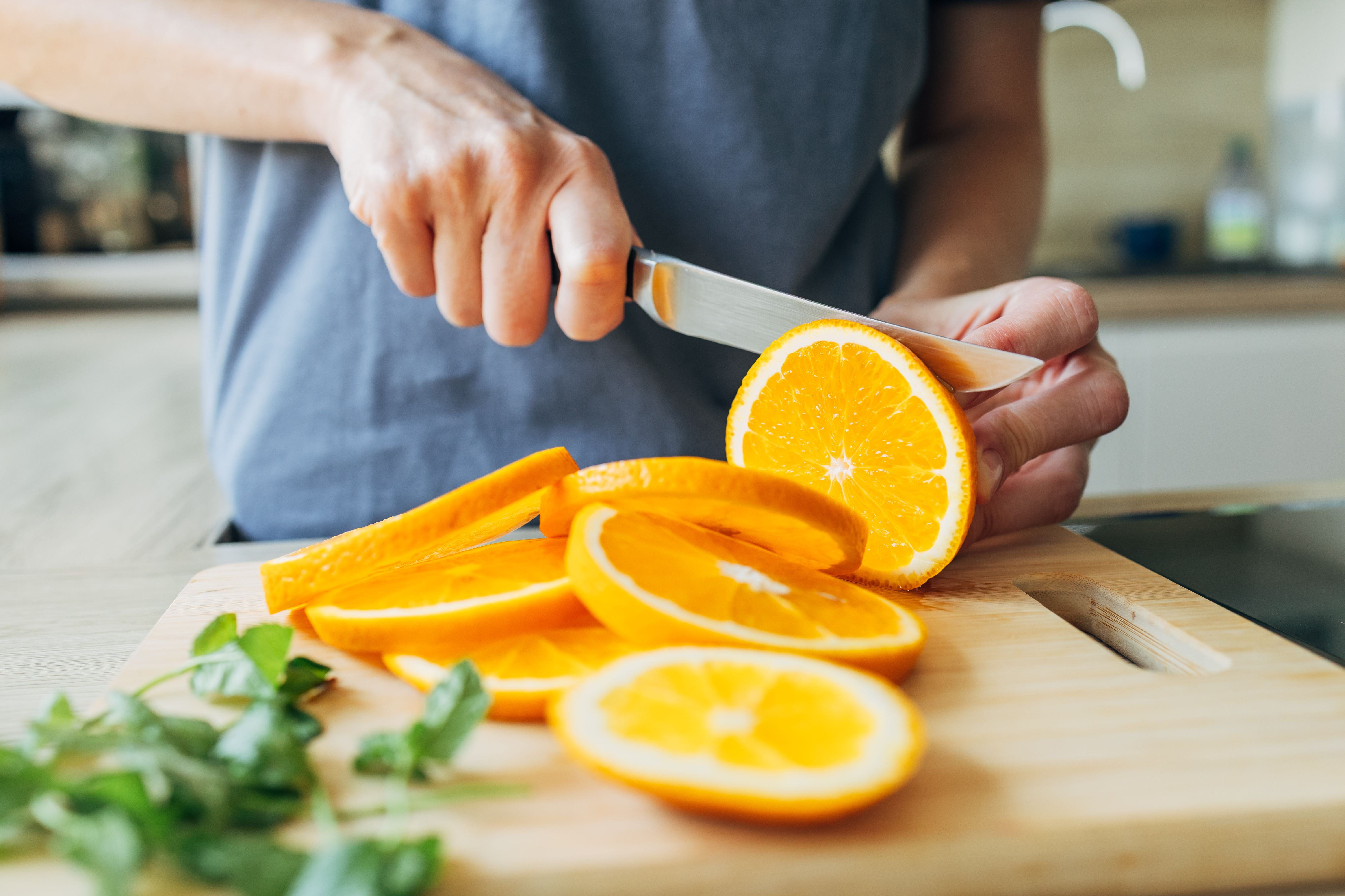 Person schneidet eine frische Orange auf einem Holzbrett in Scheiben.