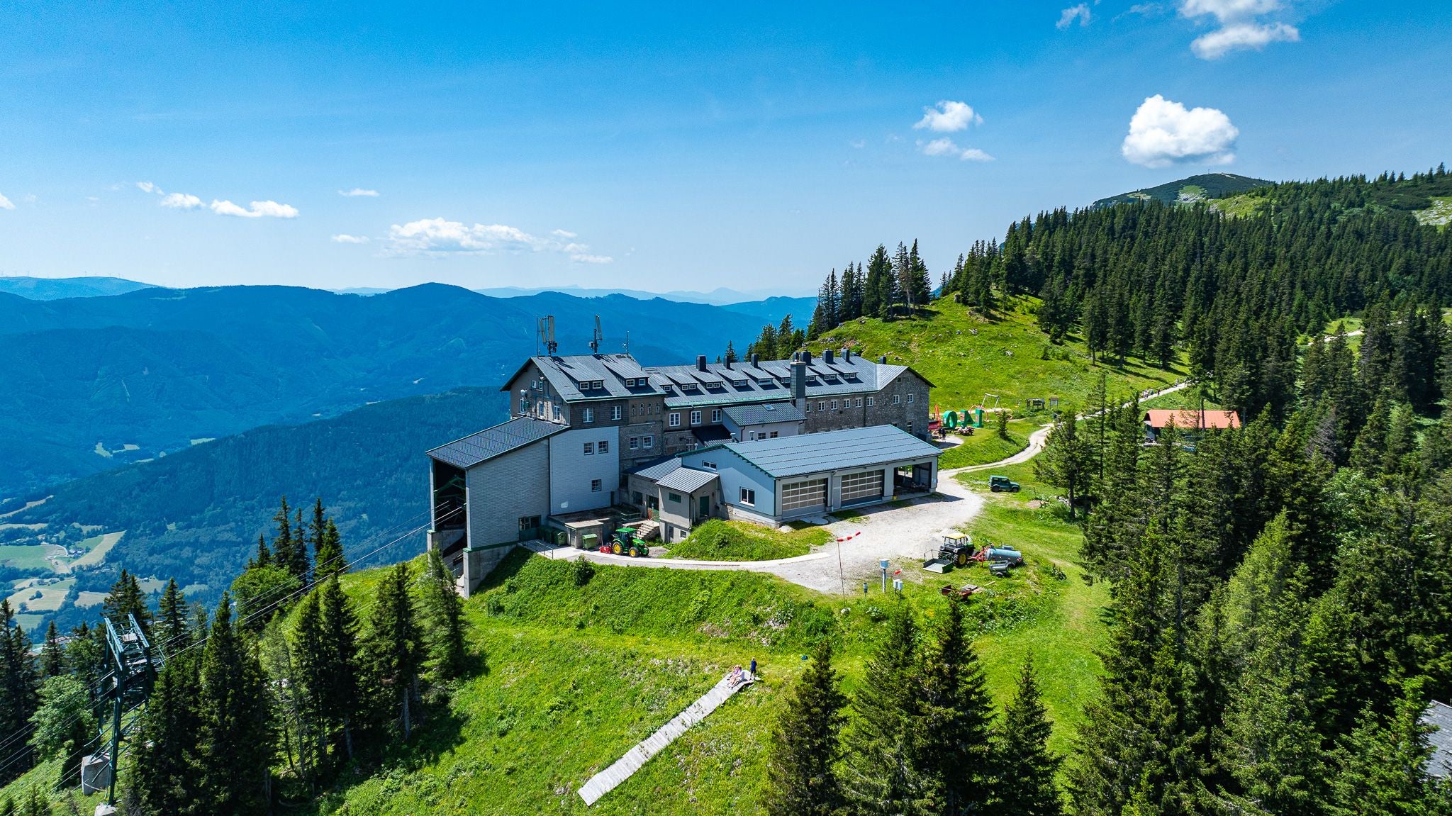 Großes Berghaus bei der Rax Seilbahn umgeben von Wäldern und Bergen unter blauem Himmel.