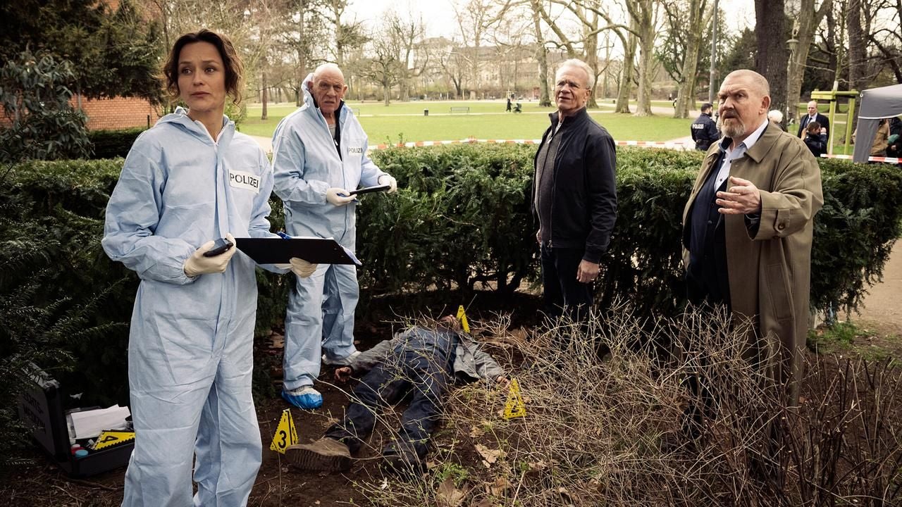 Polizisten und Ermittler stehen an einem Tatort im Park bei einer Leiche und sichern Spuren.