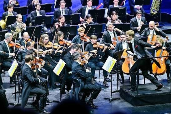 Dirigent leitet ein Orchester, das auf einer Bühne klassische Musik spielt.