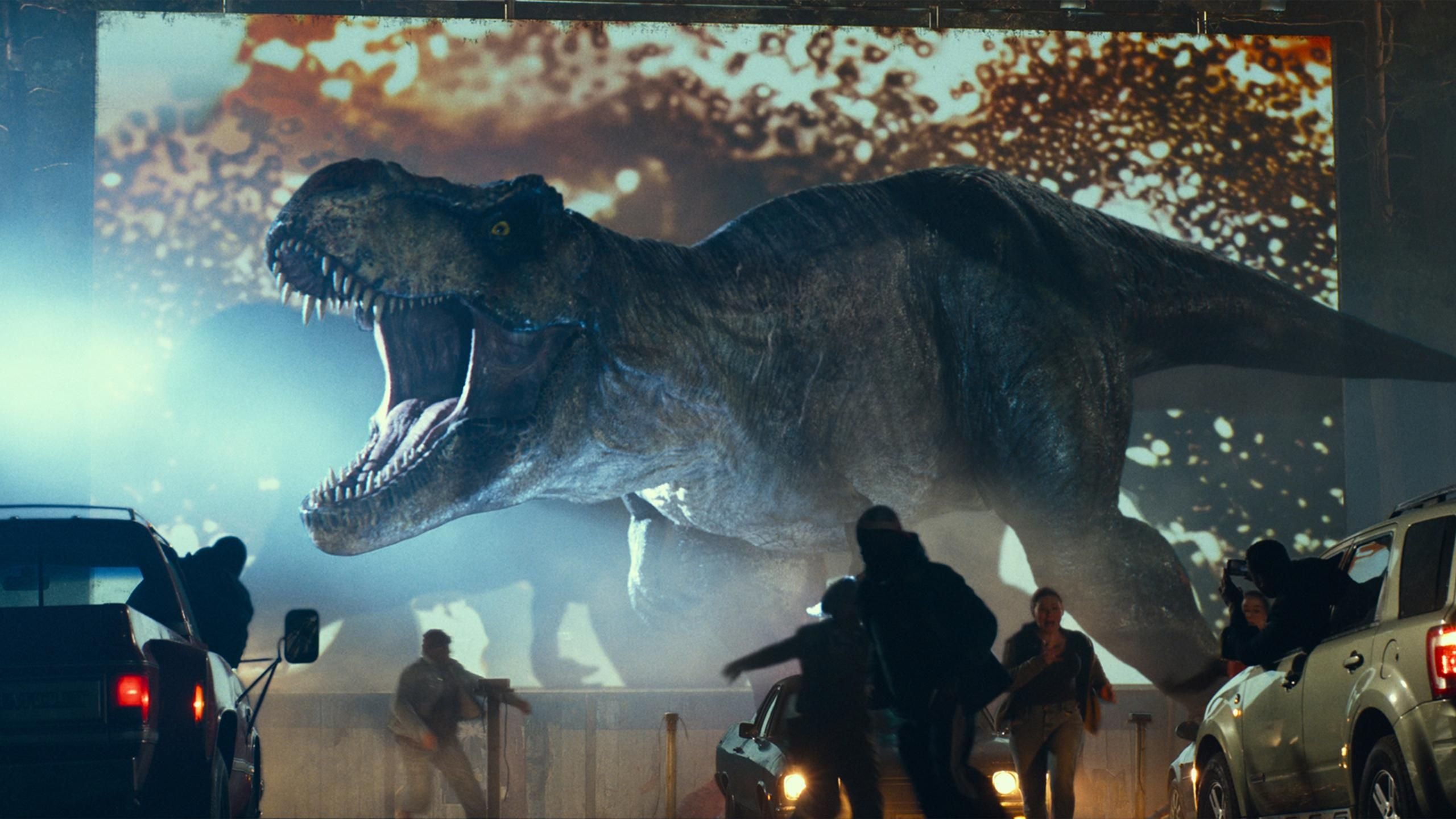 Menschen fliehen vor einer großen Dinosaurierprojektion auf einer Kinoleinwand im Freien.