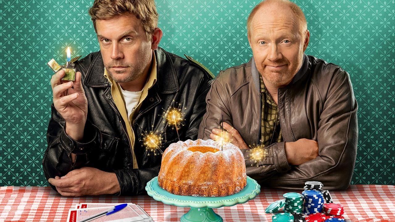 Zwei Männer sitzen an einem Tisch mit einem Kuchen mit Wunderkerzen, Pokerchips und einem Lottozettel.