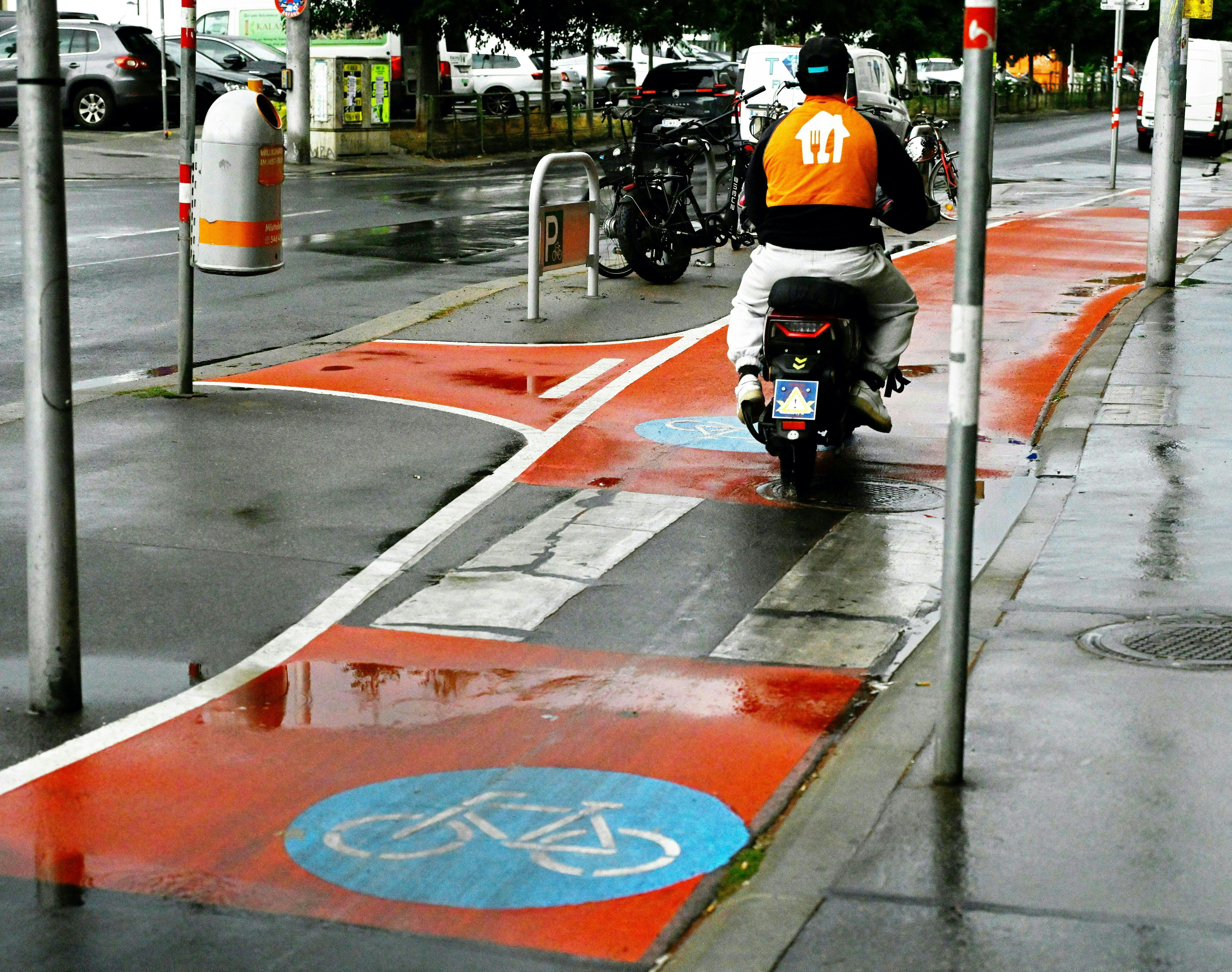 Ein Liefermoped fährt auf einem nassen Fahrradweg in Wien bei regnerischem Wetter.