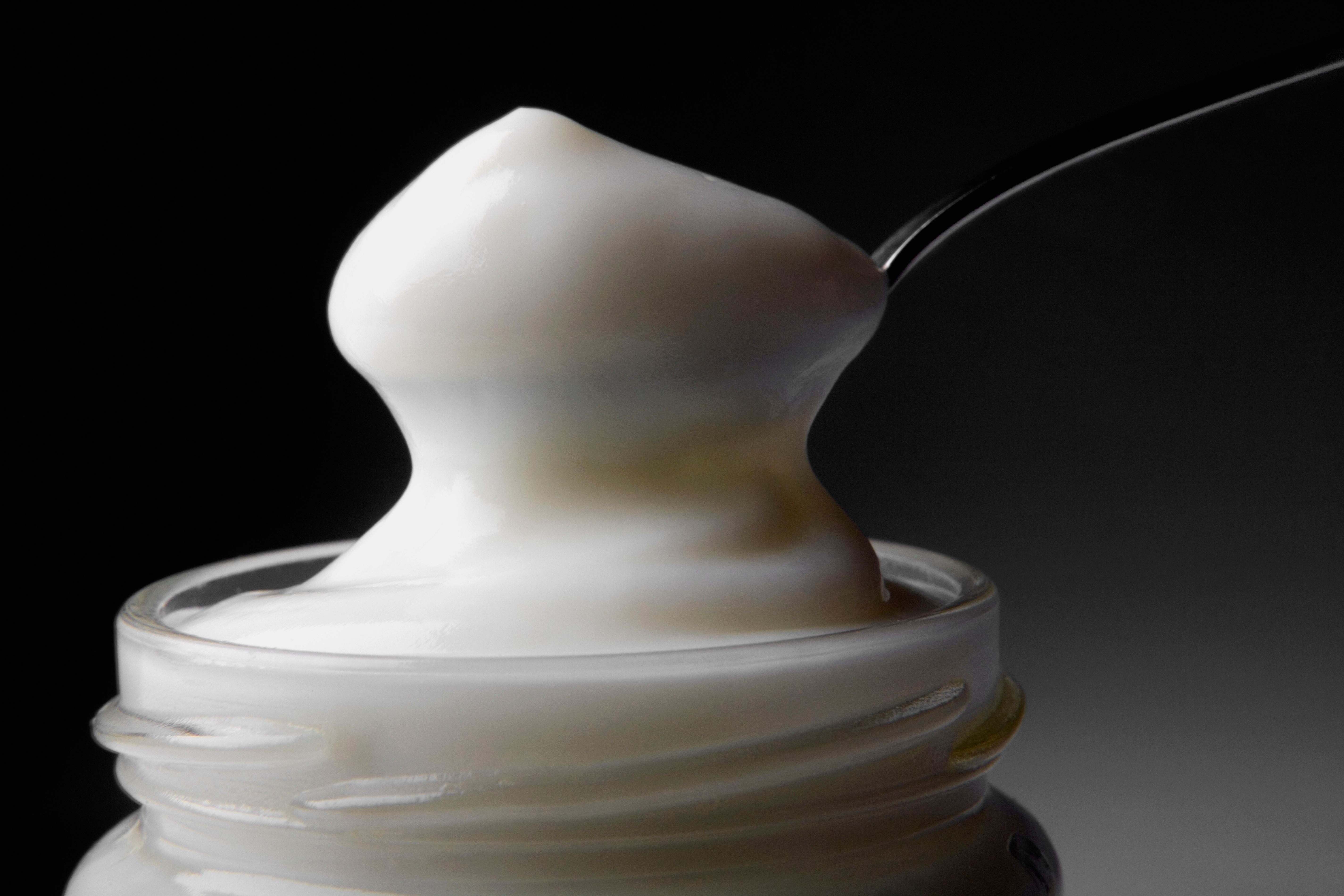 Ein Löffel mit cremiger Mayonnaise über einem Glasbehälter.