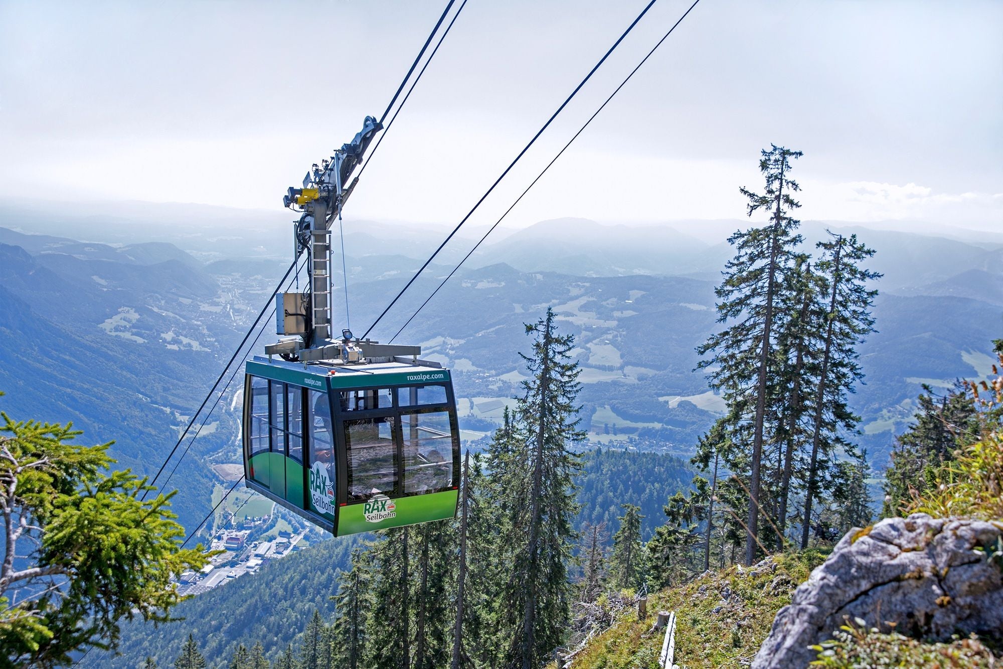 Die Rax-Seilbahn fährt über bewaldete Berghänge mit weitem Blick ins Tal und auf Berge.
