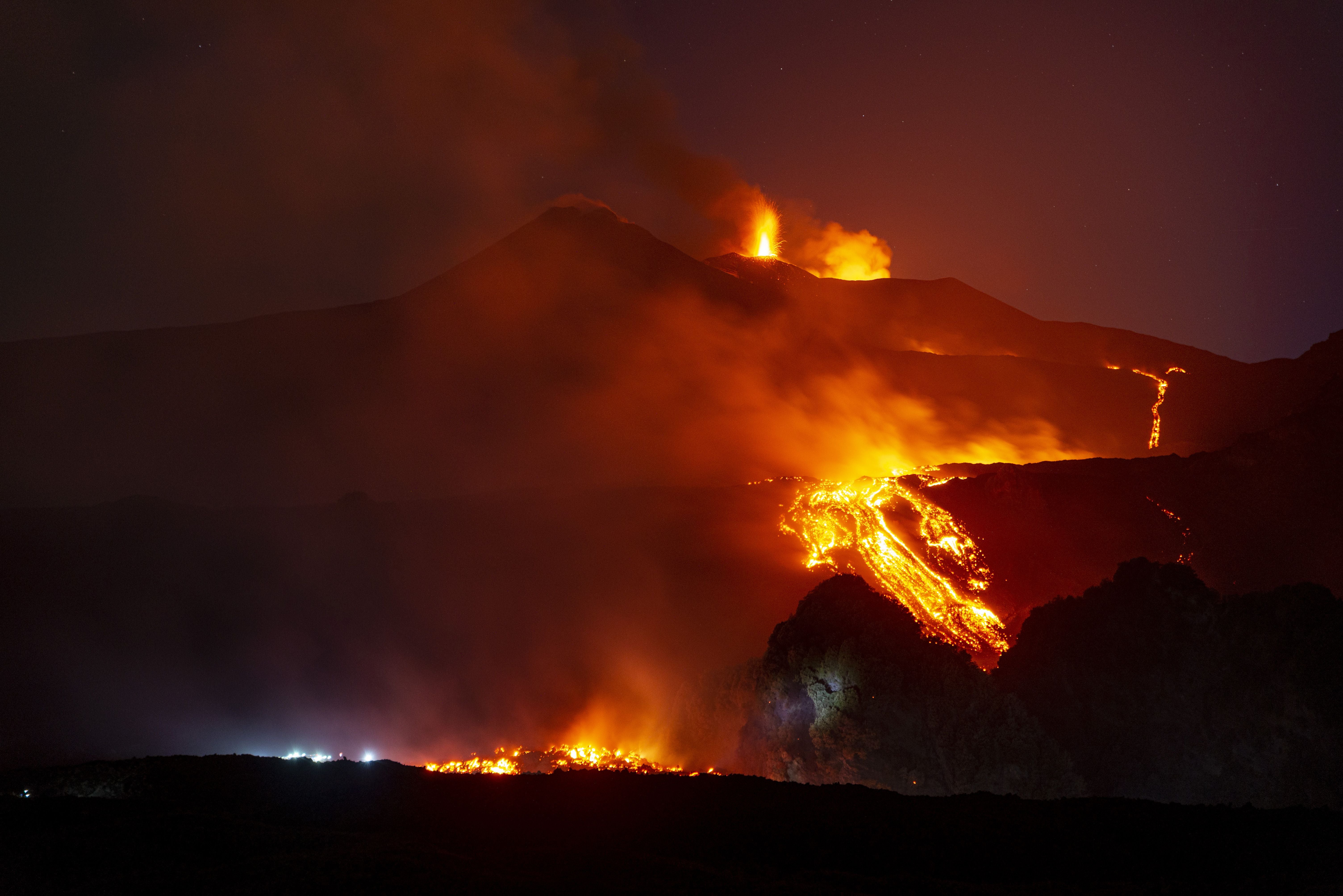 Leuchtende Lavaströme fließen bei Nacht während eines Ausbruchs vom Ätna, Rauch steigt auf.