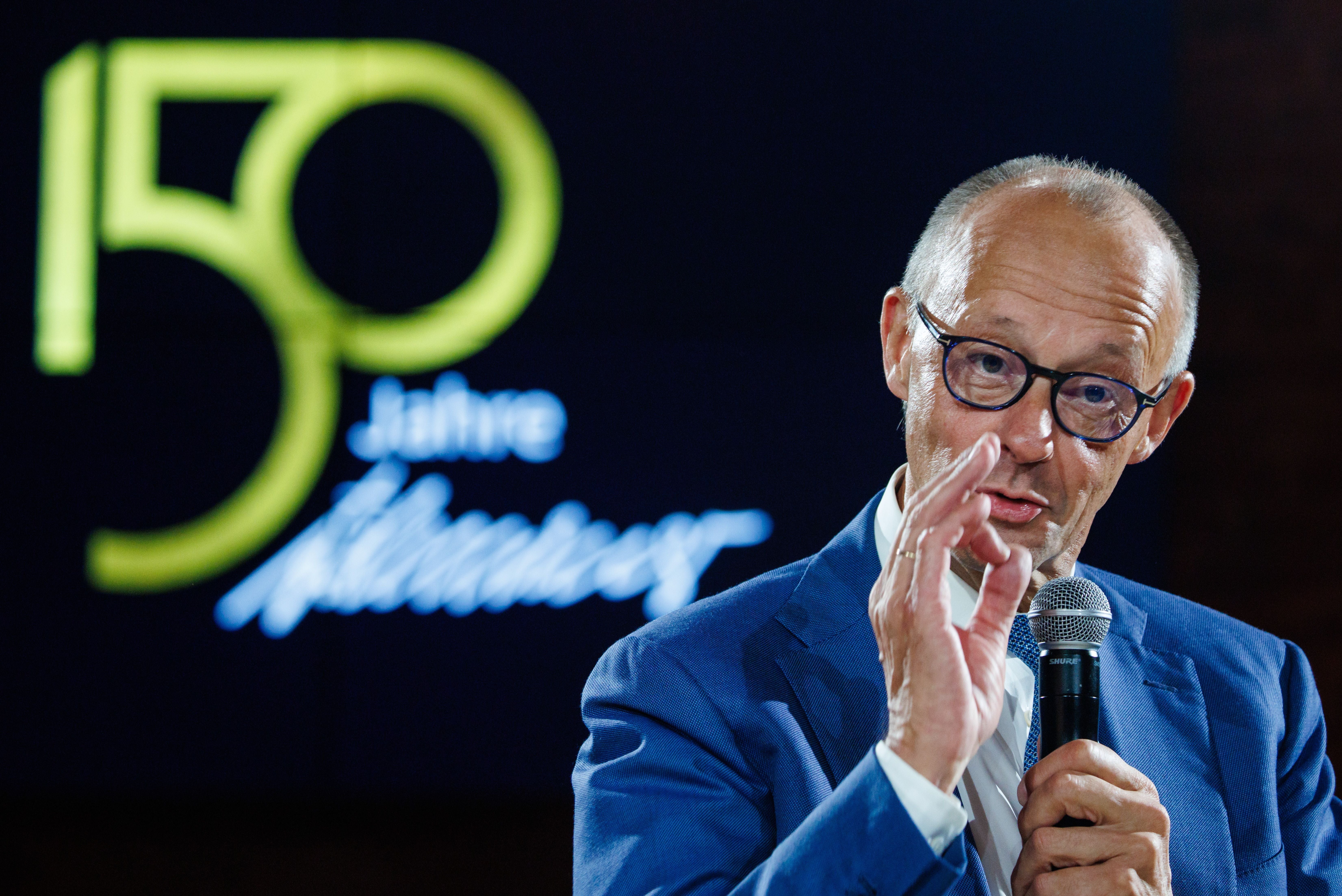 Ein Mann im blauen Anzug spricht bei einer Veranstaltung mit Mikrofon, Hintergrund "150 Jahre".