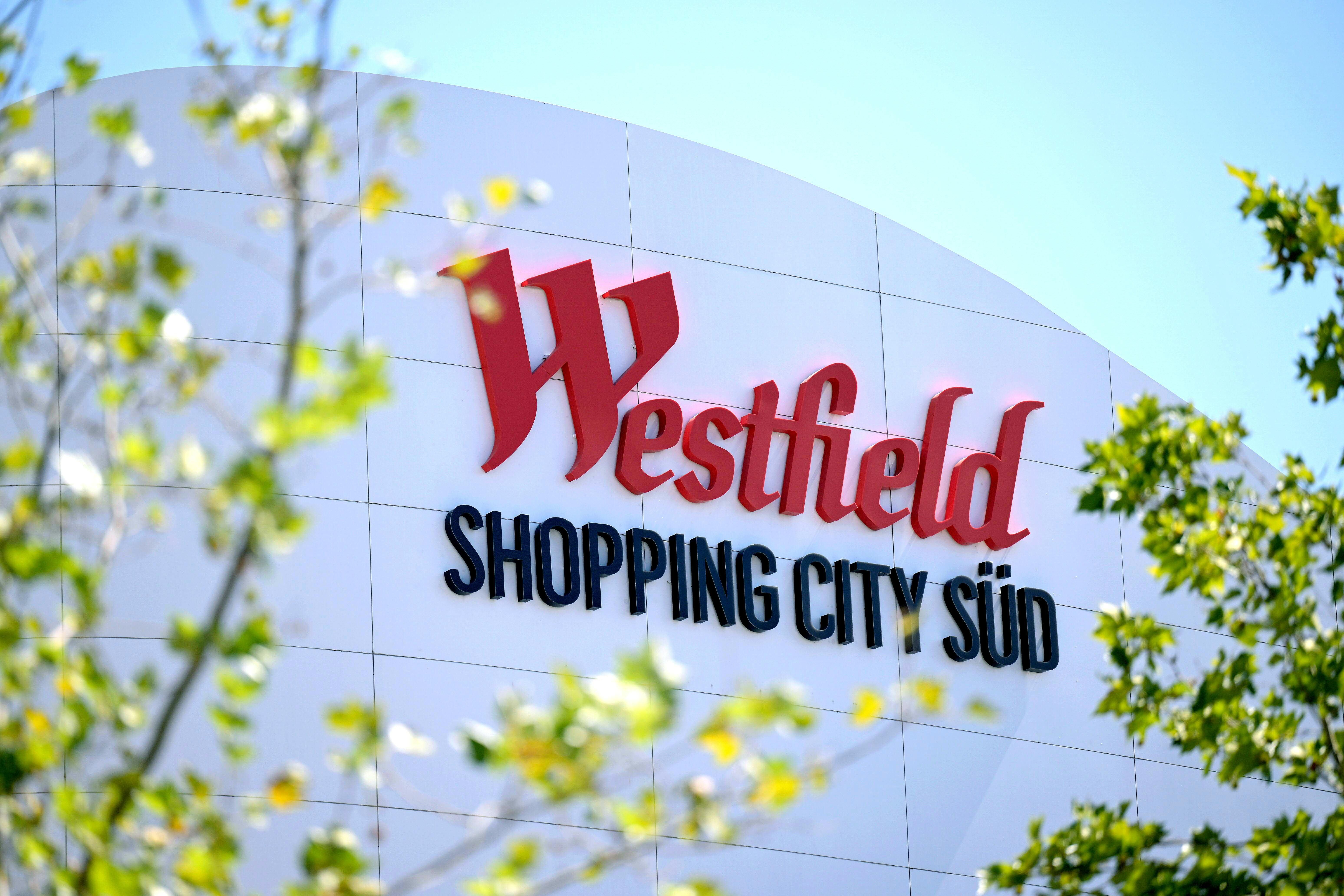 Logo von Westfield Shopping City Süd an einer Fassade, umgeben von grünen Zweigen.