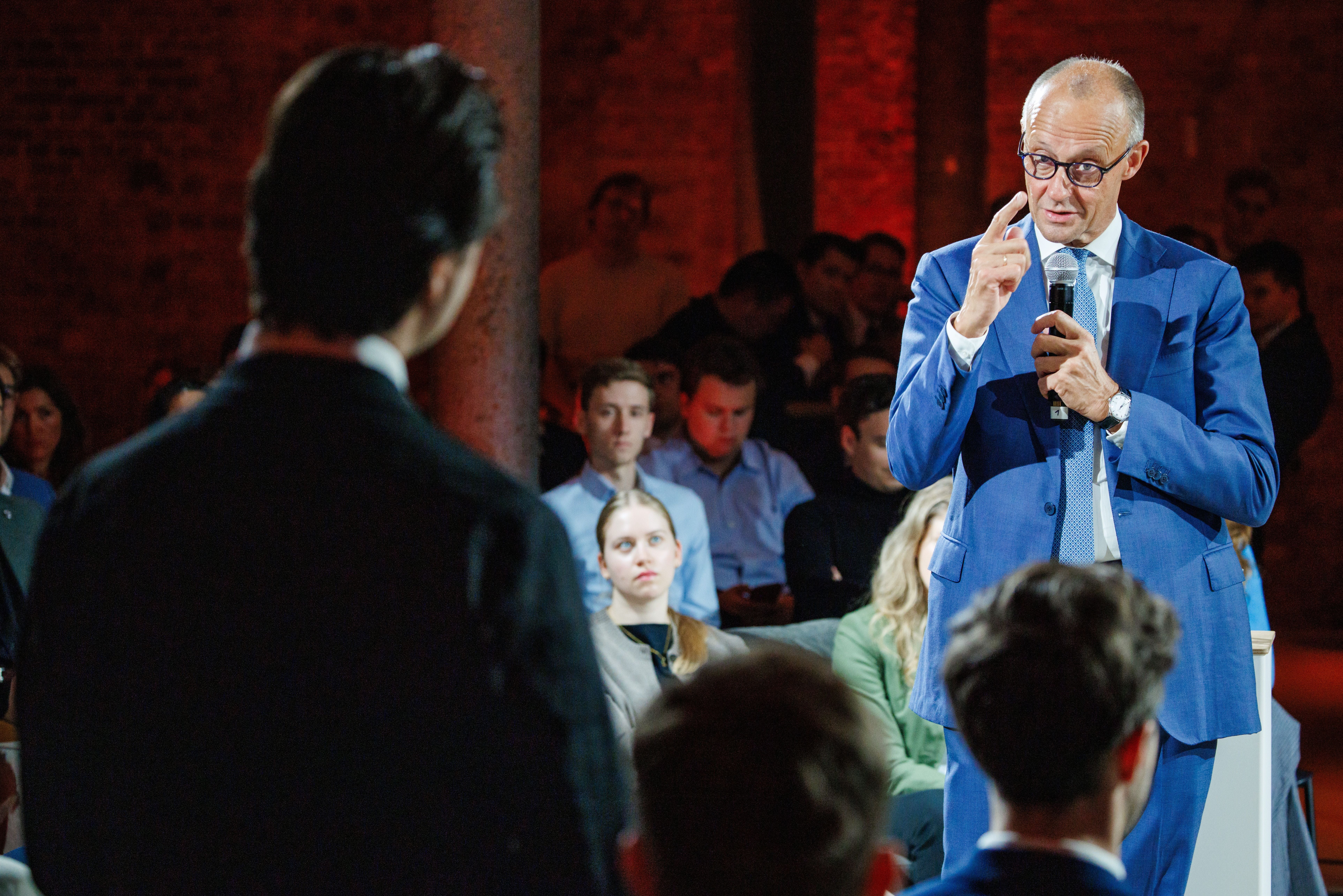 Ein Mann im blauen Anzug spricht mit Mikrofon vor Publikum bei einer Podiumsdiskussion.