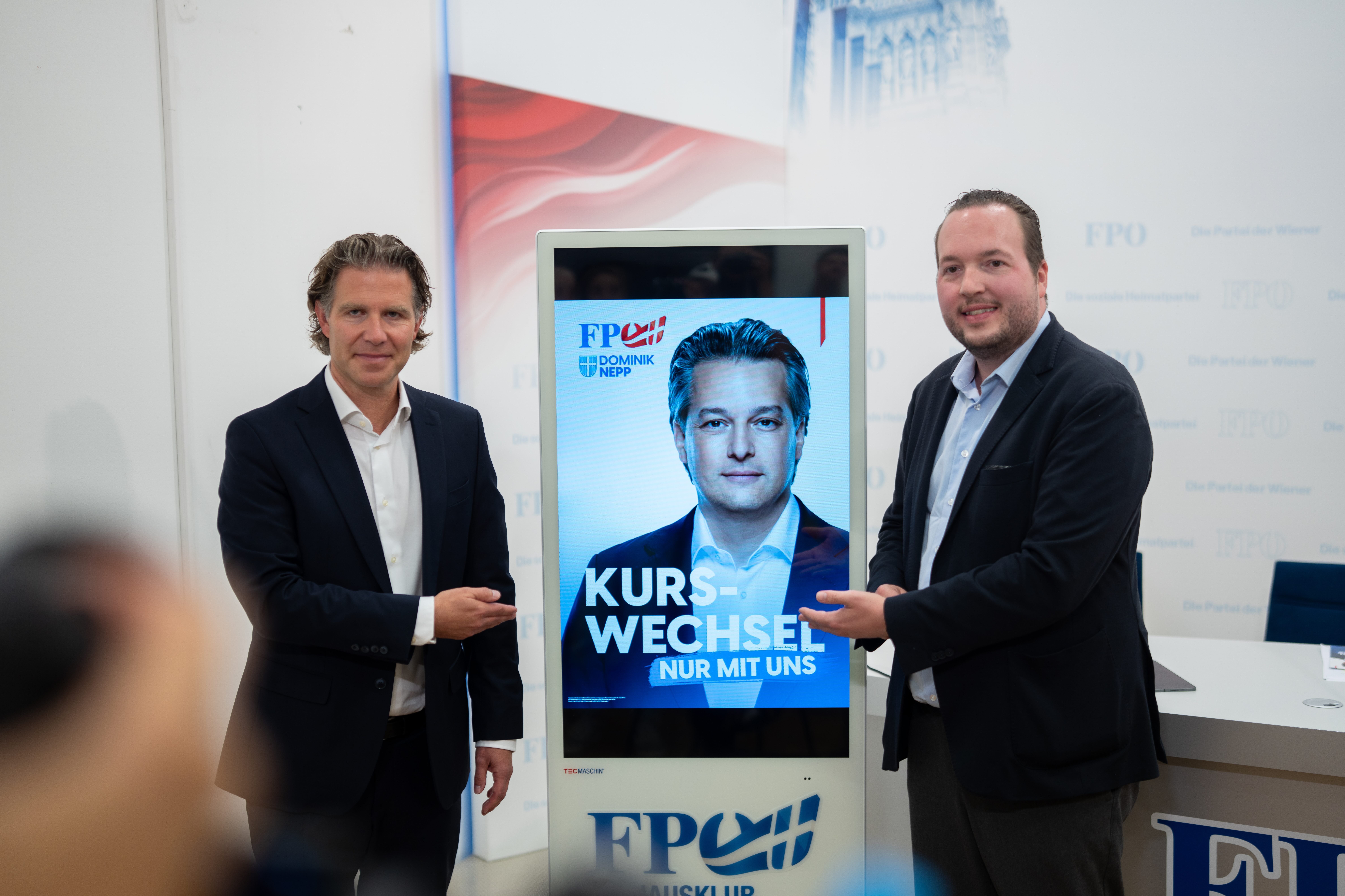 Zwei Männer präsentieren ein Wahlplakat der FPÖ mit dem Slogan „Kurswechsel. Nur mit uns“.