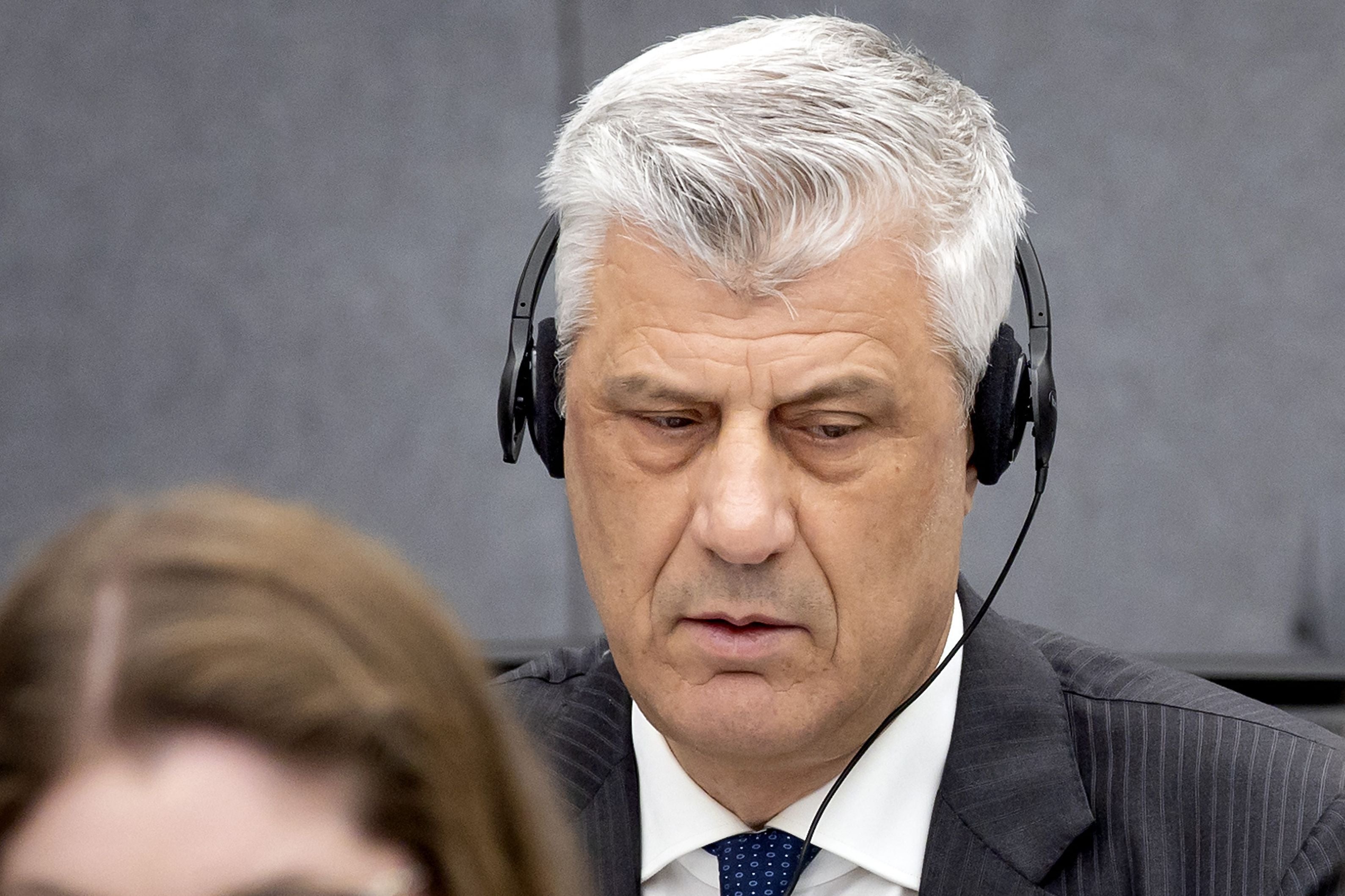 Ein Mann mit grauen Haaren trägt einen Anzug und Kopfhörer und sitzt in einem Gerichtssaal.