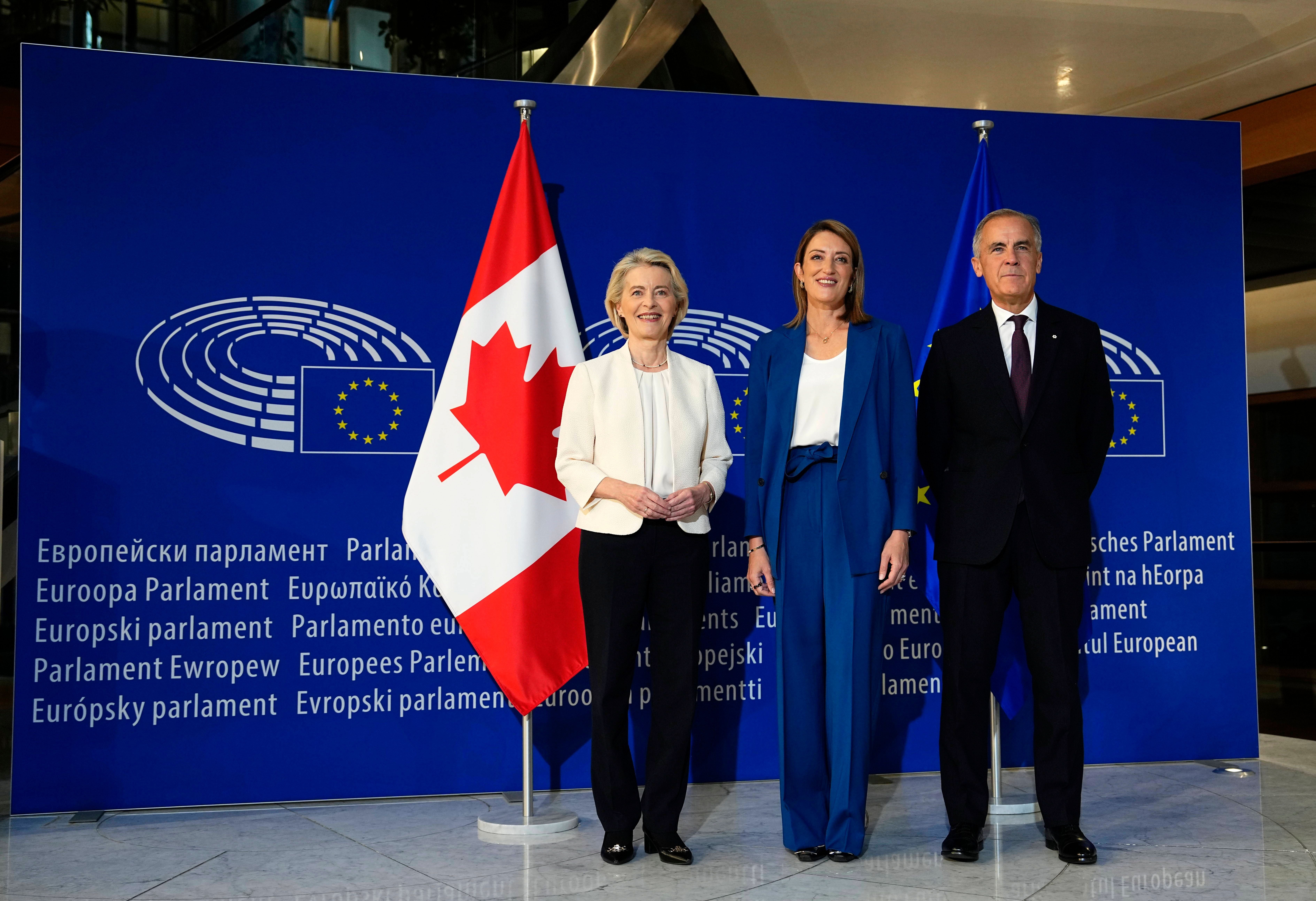 Drei Personen stehen vor EU-Logo und Flaggen von Kanada und der EU im Europäischen Parlament.