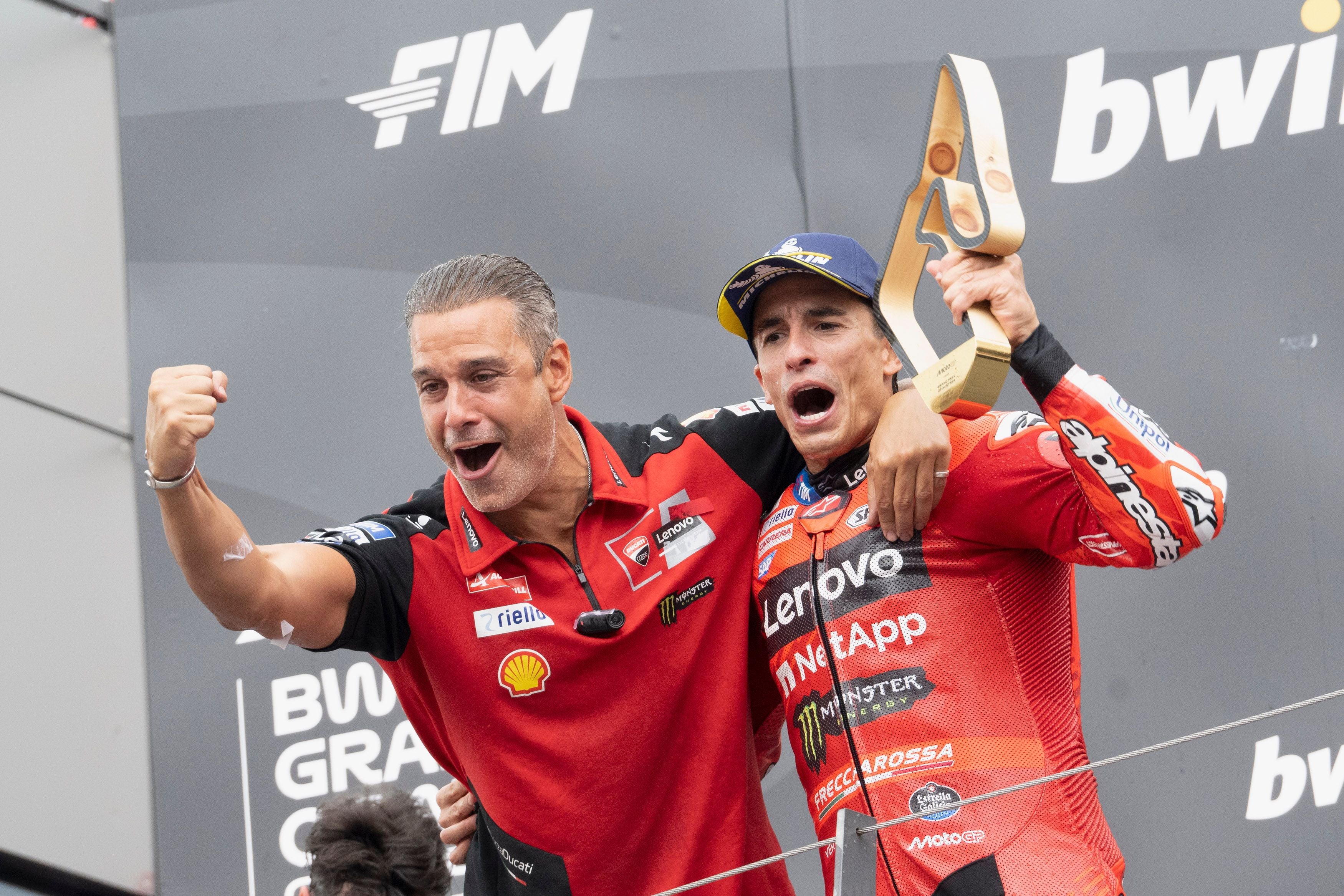 Zwei Männer jubeln auf dem Podium, einer hält eine Trophäe, beide tragen Ducati-Teamkleidung.