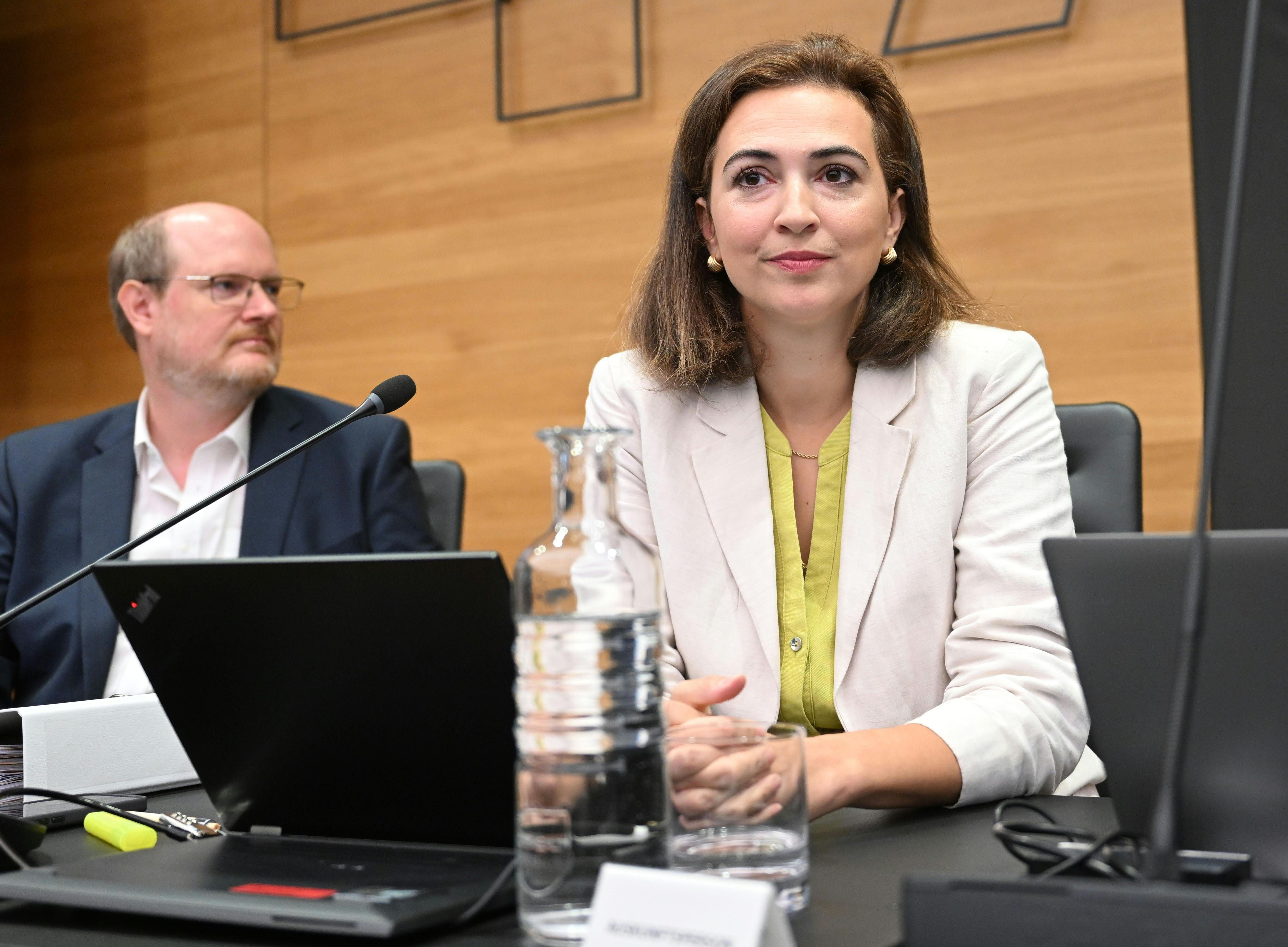 Zwei Personen sitzen bei einer Ausschusssitzung im Parlament an einem Tisch mit Laptops und Mikrofon.