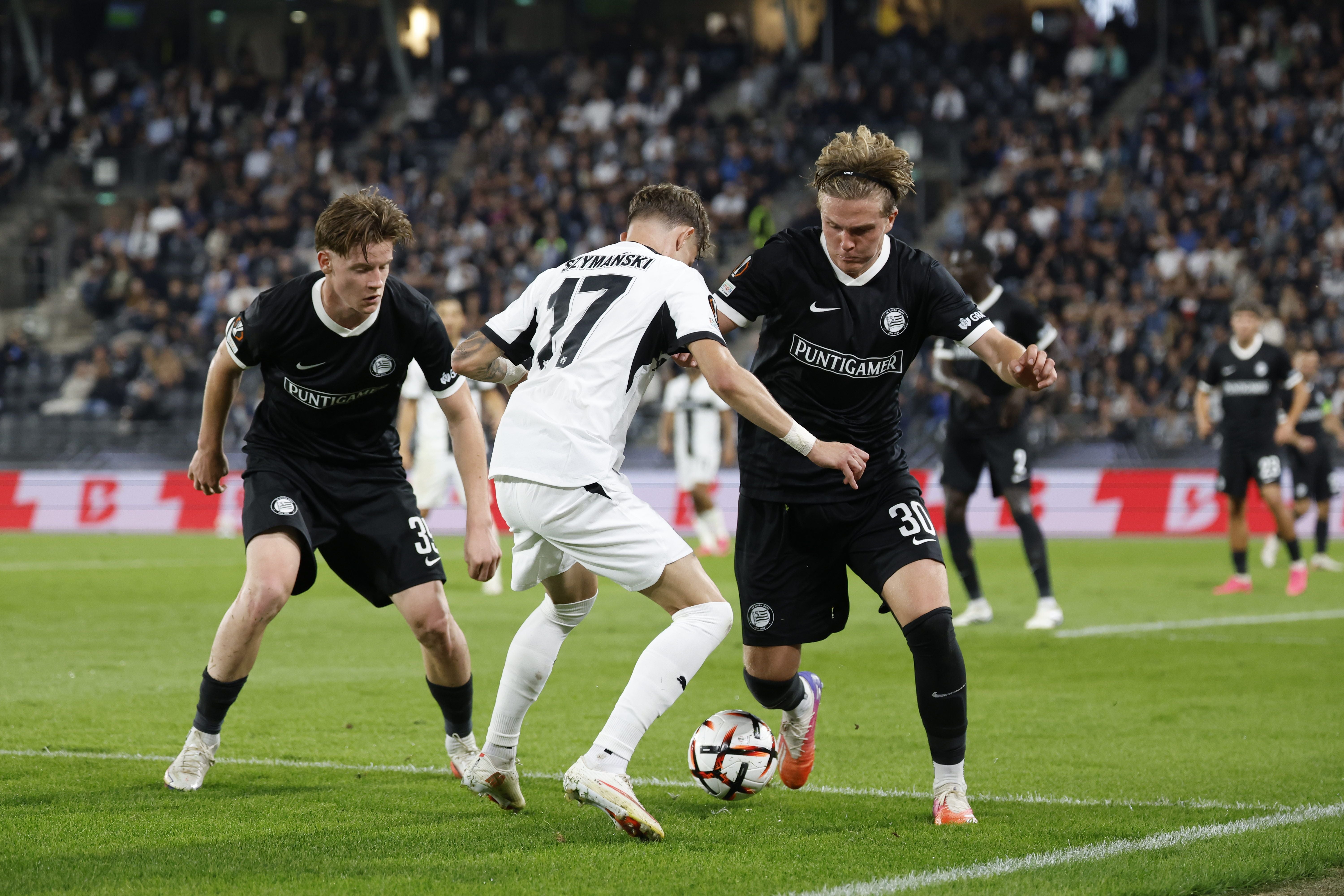 Zwei Spieler in schwarzen Trikots und ein Spieler in weiß kämpfen im Strafraum um den Ball.