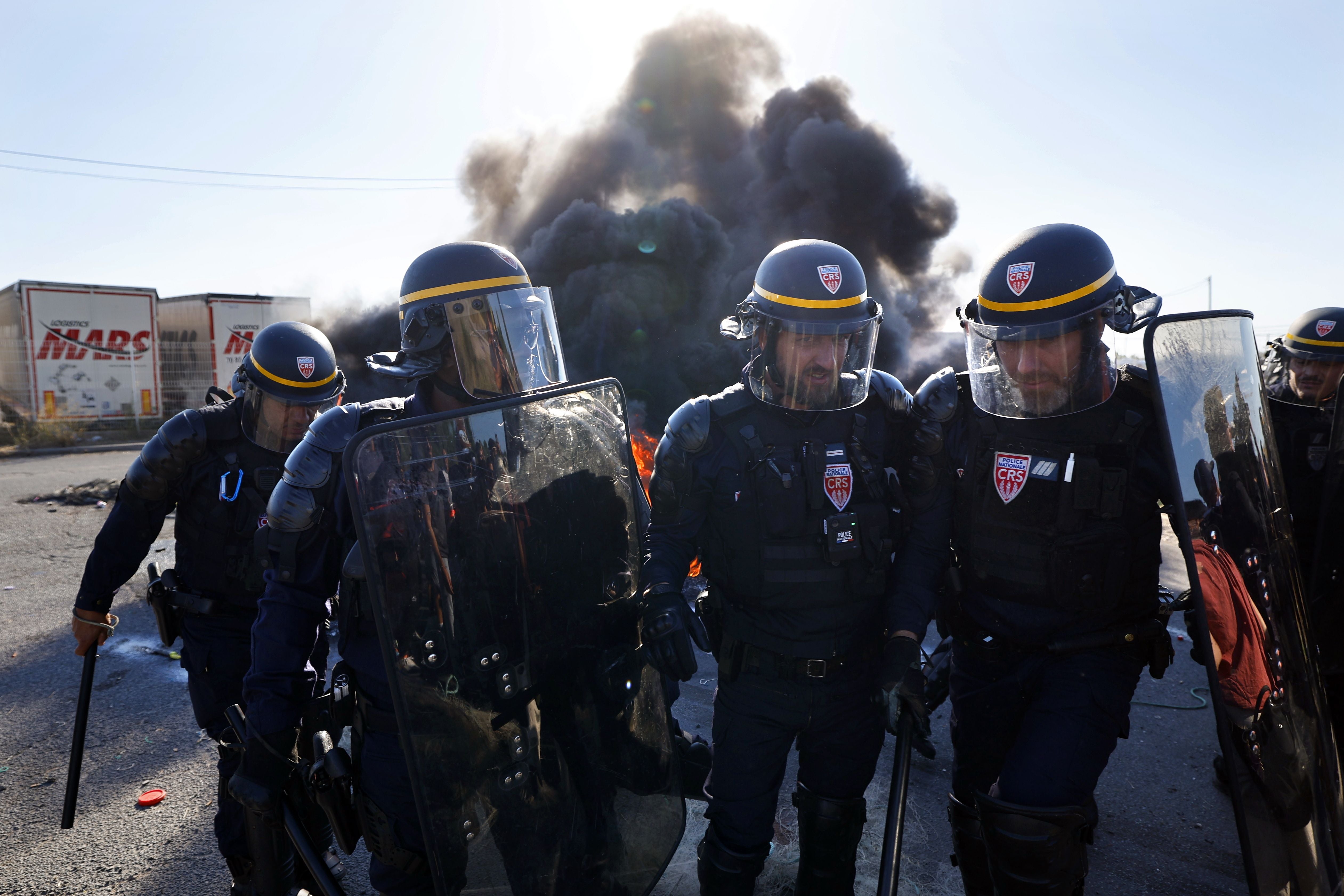 Polizisten in Schutzkleidung vor brennenden Barrikaden und Rauch während einer Demonstration.