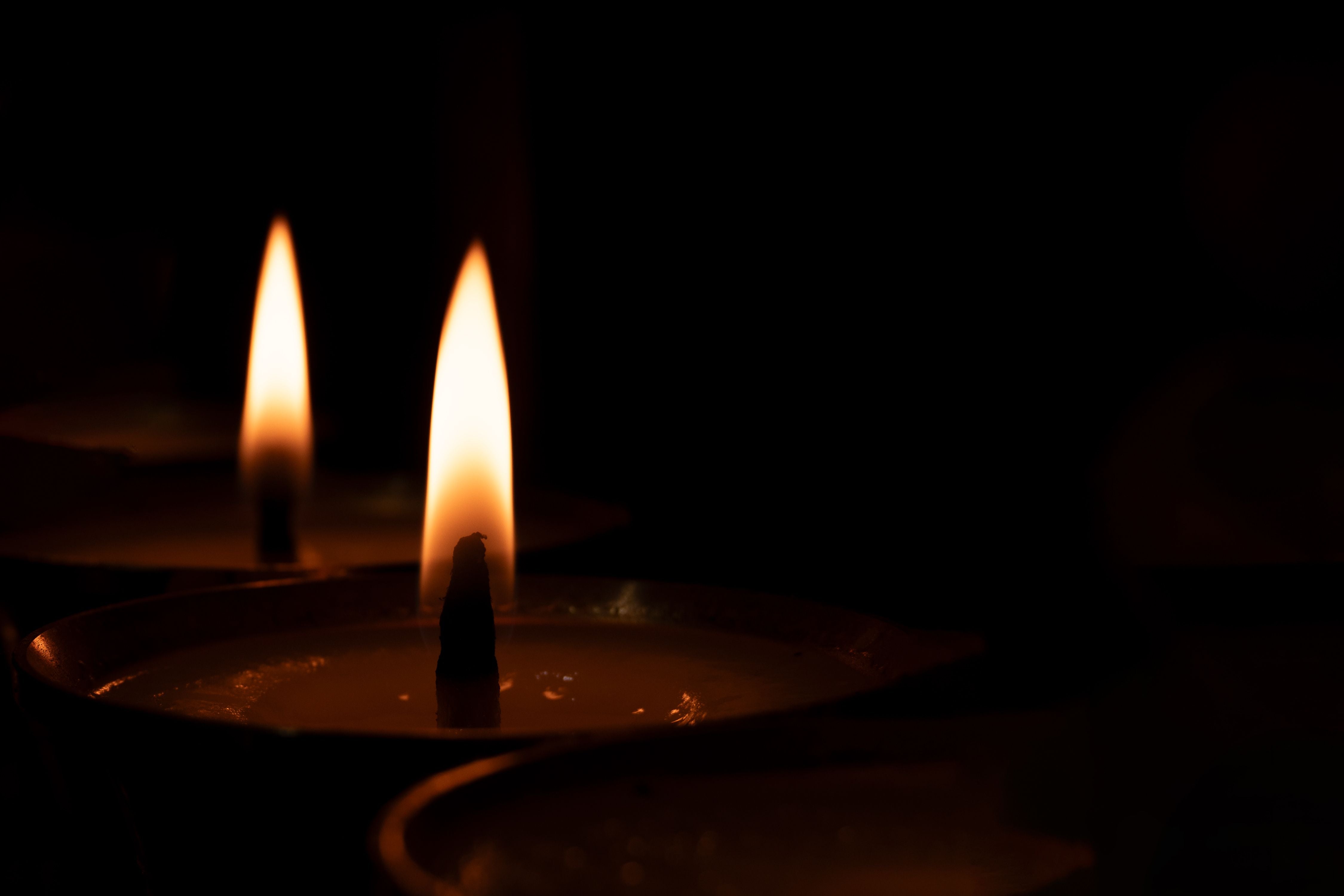 Zwei Teelichter mit Flamme leuchten im Dunkeln vor schwarzem Hintergrund.