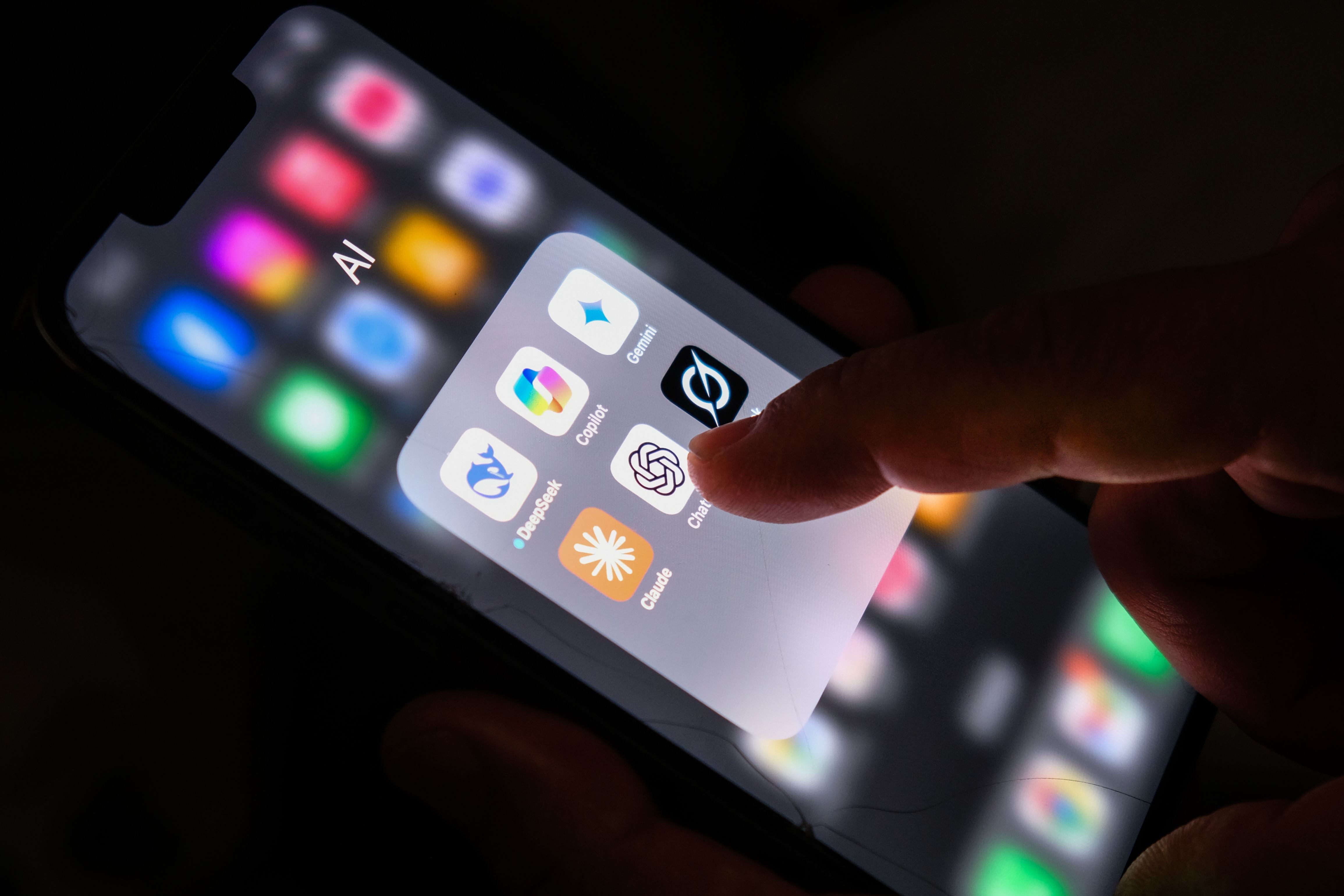 Finger tippt auf AI-App-Ordner mit ChatGPT, DeepSeek, Gemini, Copilot, Grok und Claude auf iPhone.