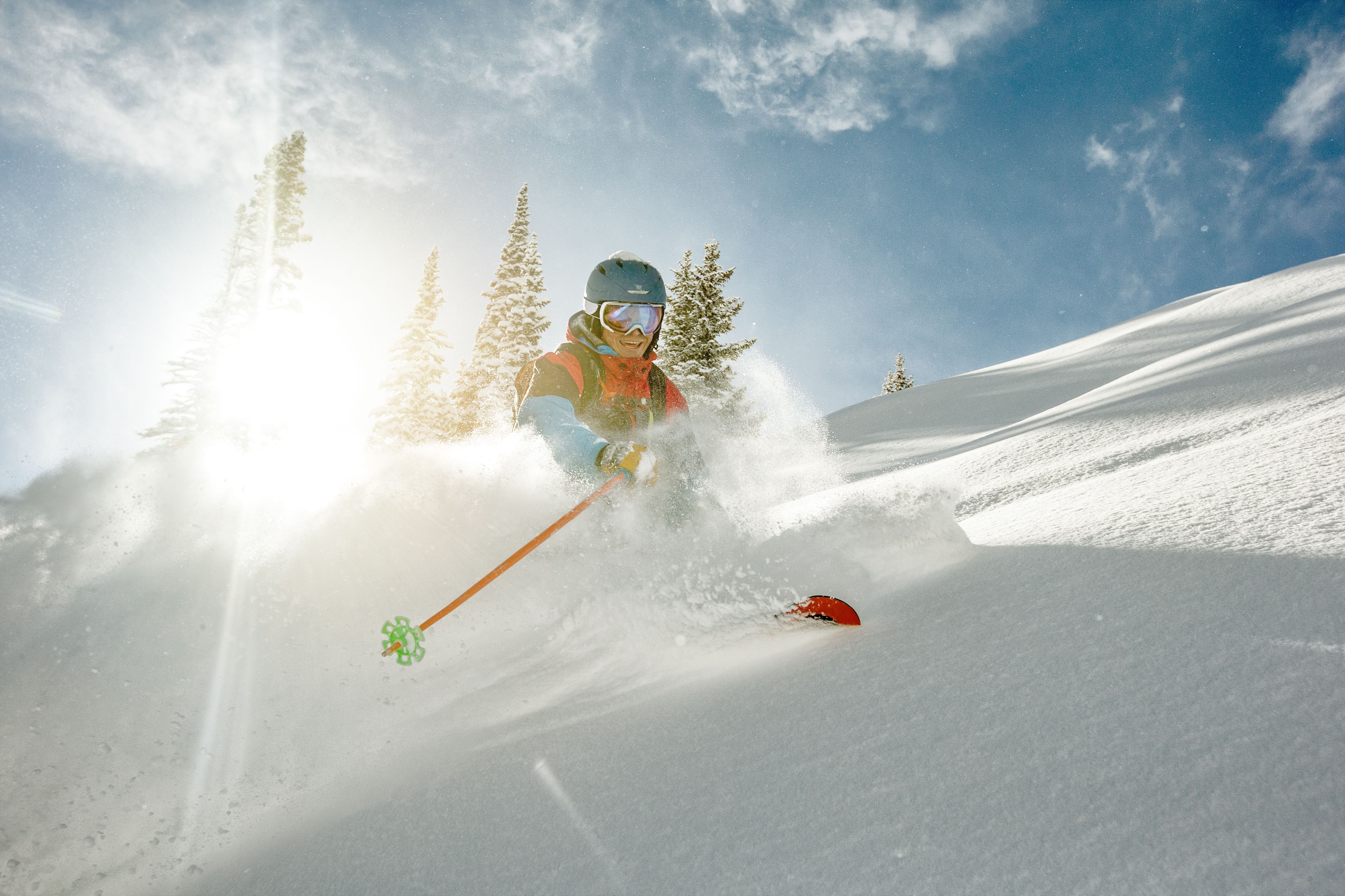 Skifahrer fährt durch frischen Pulverschnee bei Sonnenschein und blauem Himmel.
