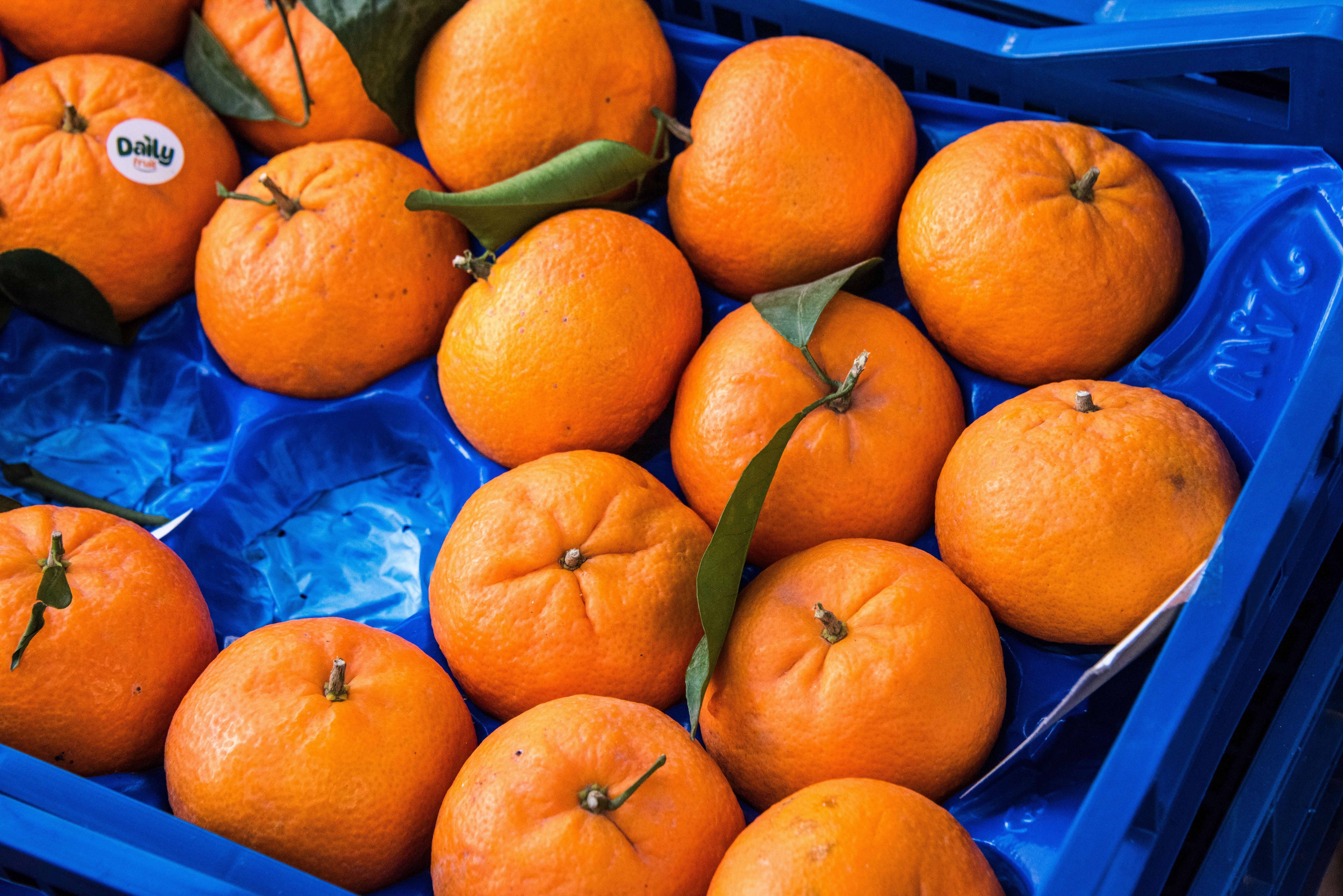 Frische Clementinen mit grünen Blättern liegen in einer blauen Obstkiste auf einem Markt.