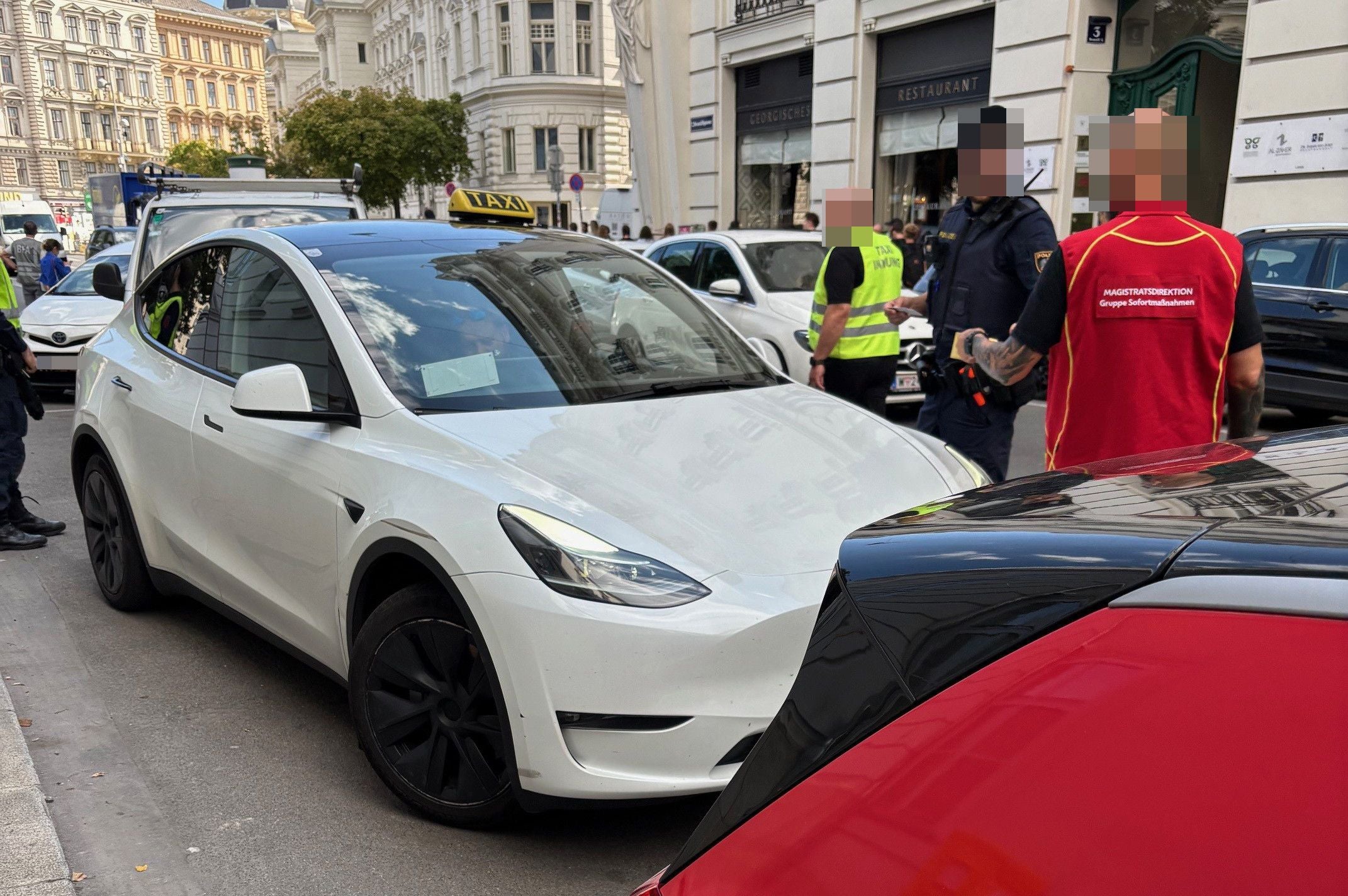 Weiße Taxi Tesla und Kontrollteam bei einer Verkehrskontrolle in einer Wiener Innenstadtstraße.