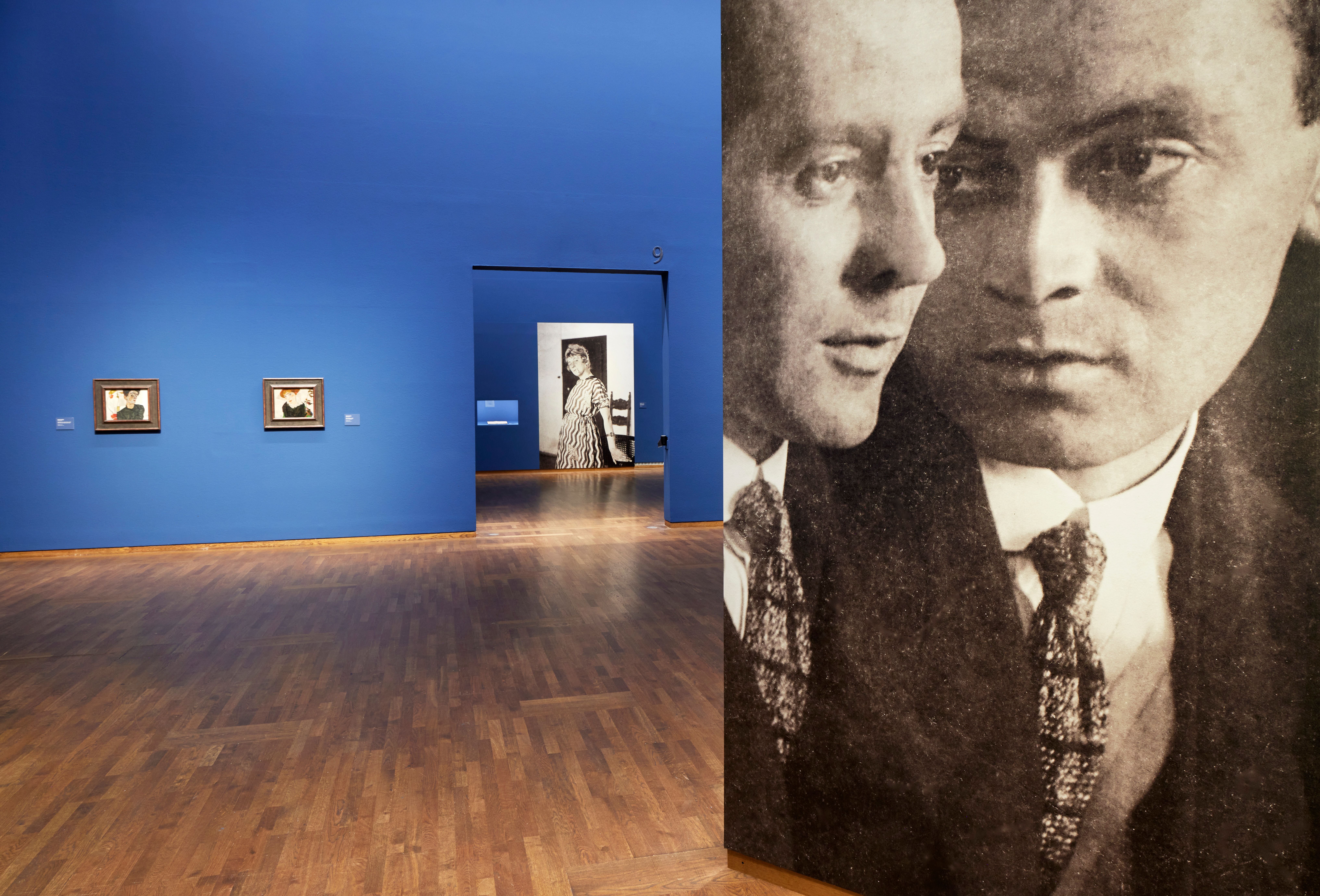 Blick in eine Kunstausstellung mit blauen Wänden und großformatigen Schwarz-Weiß-Fotografien.