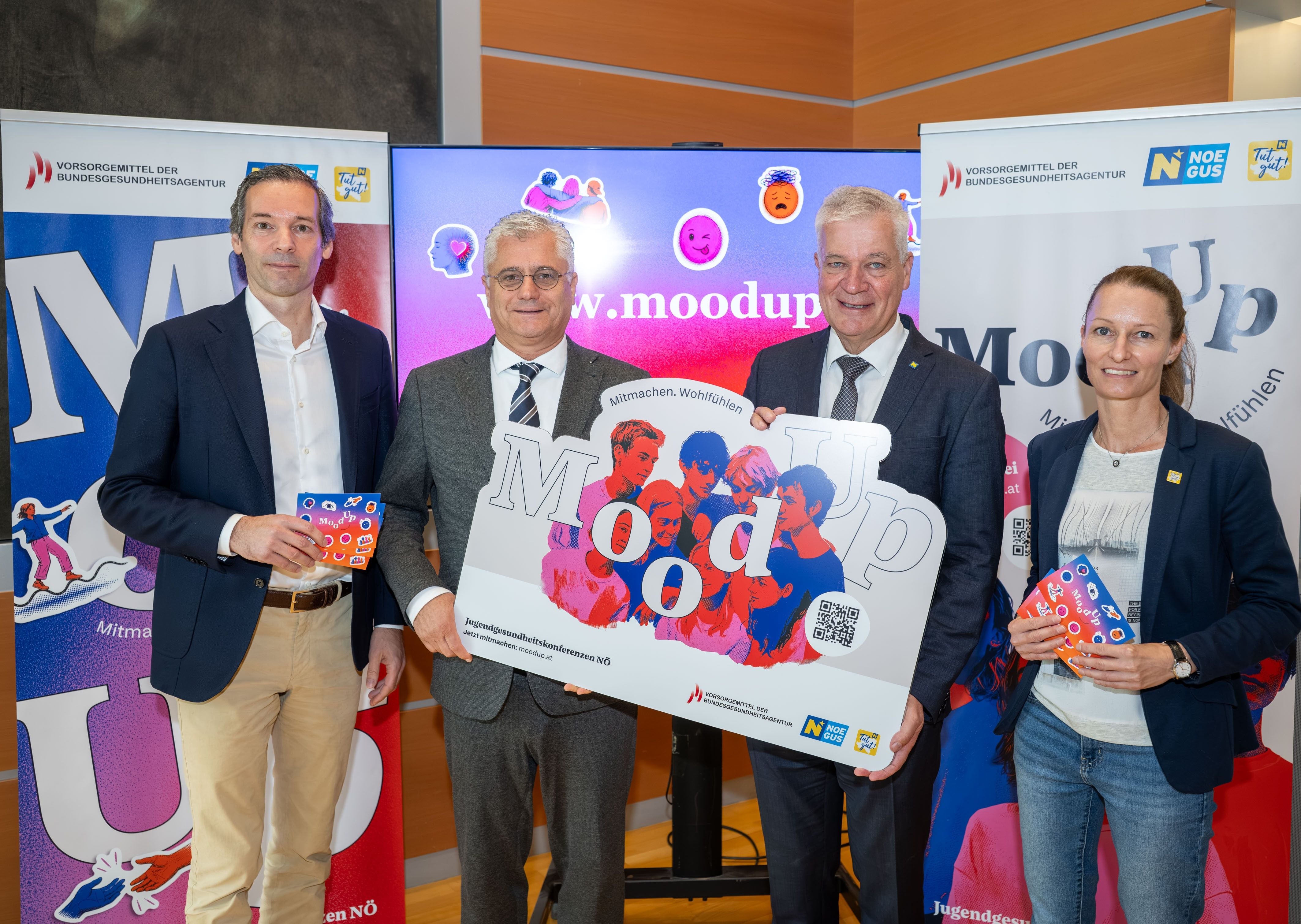 Vier Personen stehen vor Werbetafeln und halten MoodUp-Schilder und Infomaterialien in den Händen.
