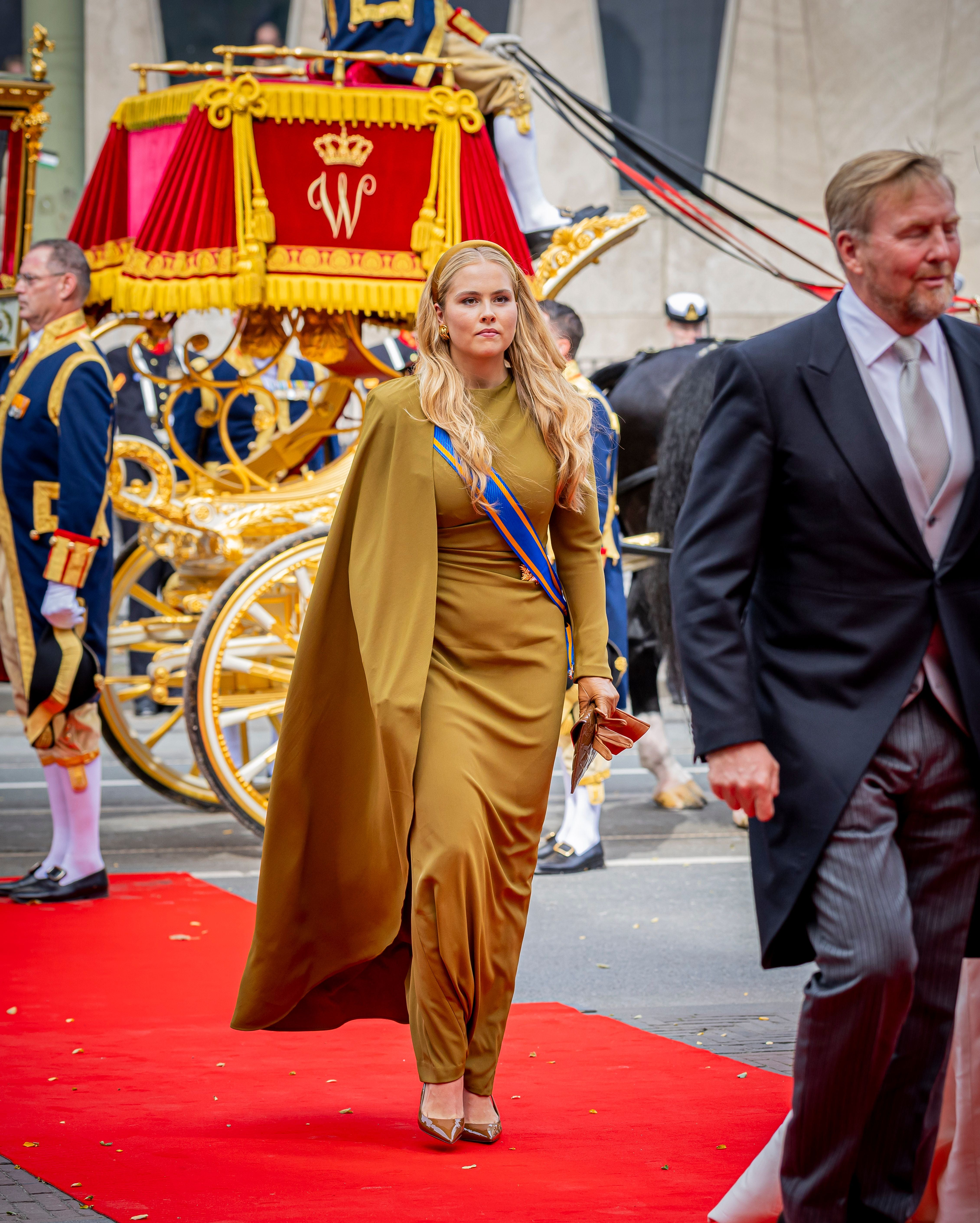 Prinzessin Amalia in goldfarbenem Kleid auf rotem Teppich mit Kutsche im Hintergrund.