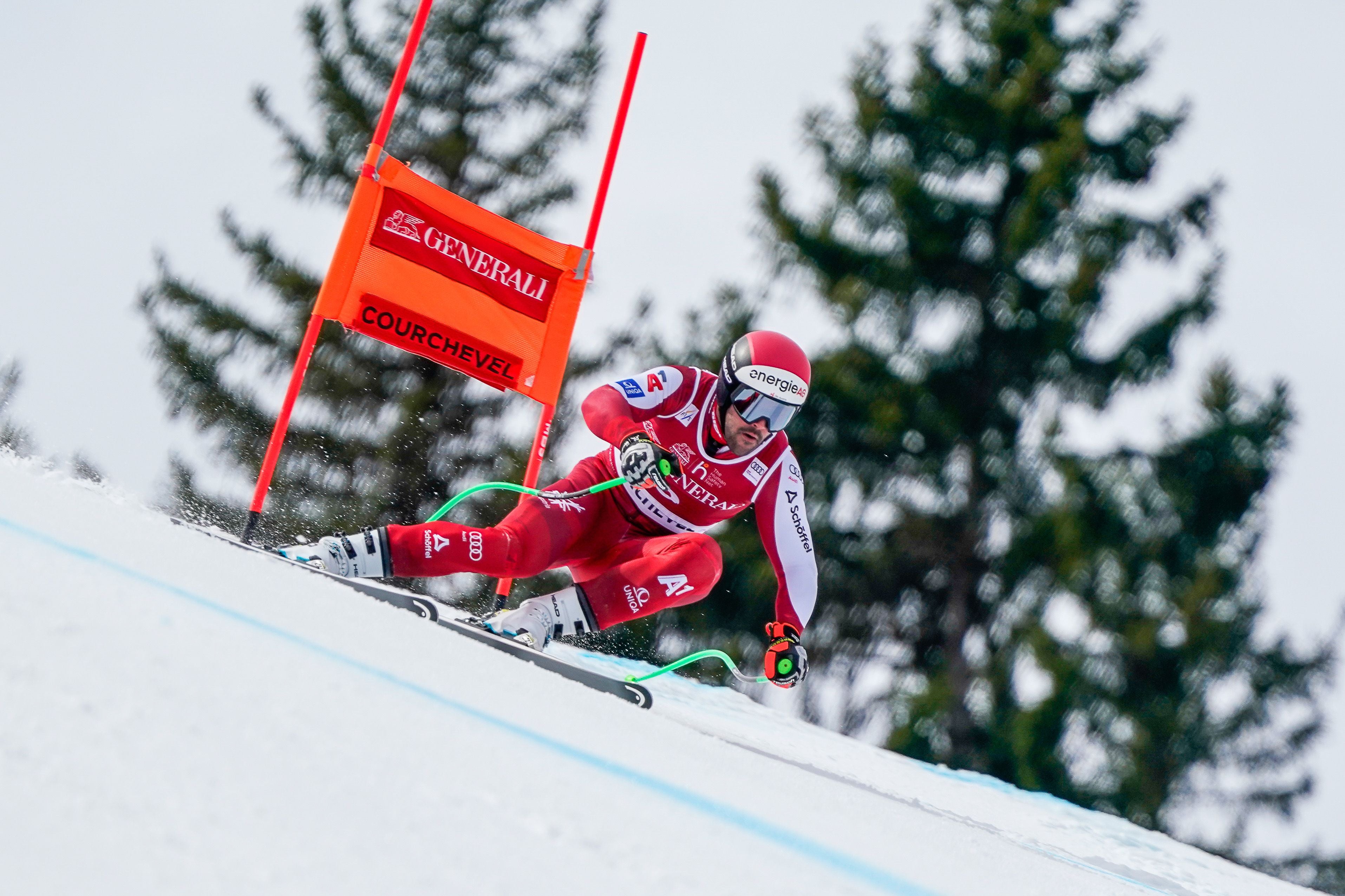 Ein Skifahrer im roten Anzug fährt beim Abfahrtslauf an einer orangefarbenen Fahne vorbei.