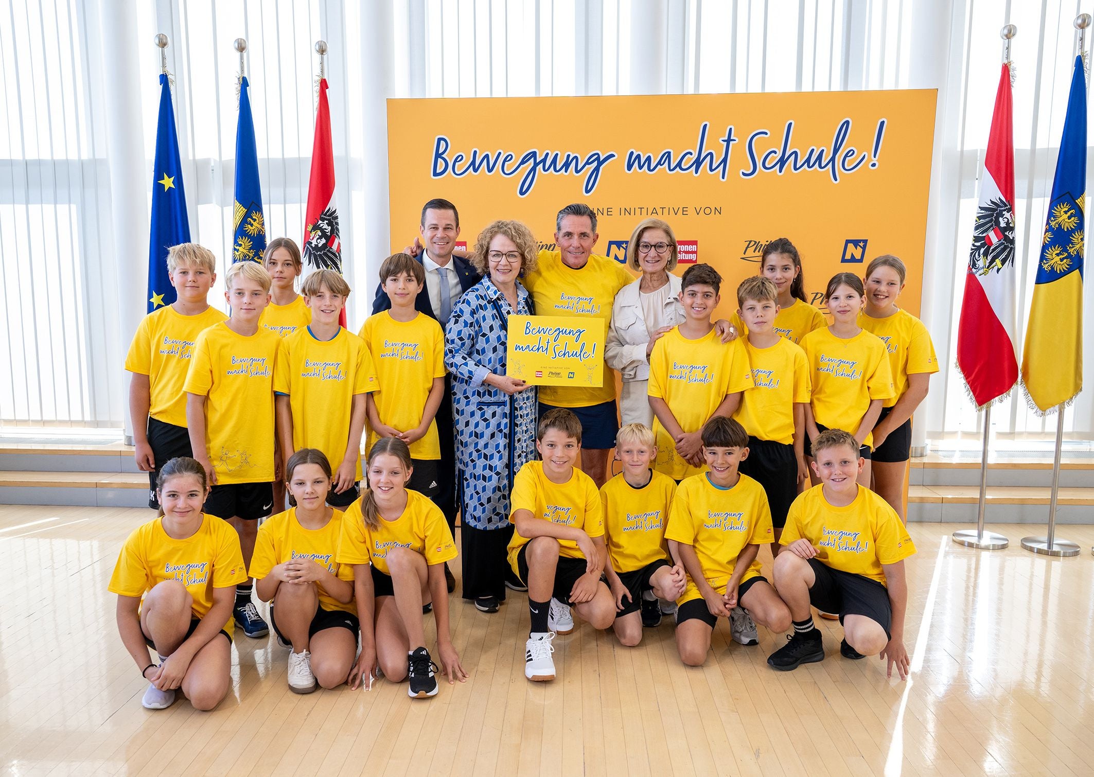 Eine Gruppe von Kindern und Erwachsenen in gelben T-Shirts posiert vor einem gelben Plakat.