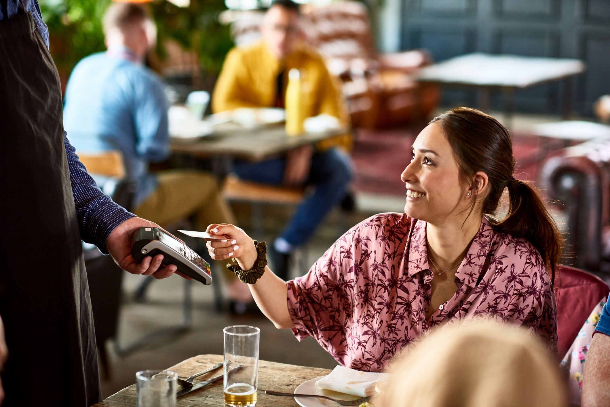 Frau zahlt lächelnd mit Karte bei einem Kellner in einem Restaurant.
