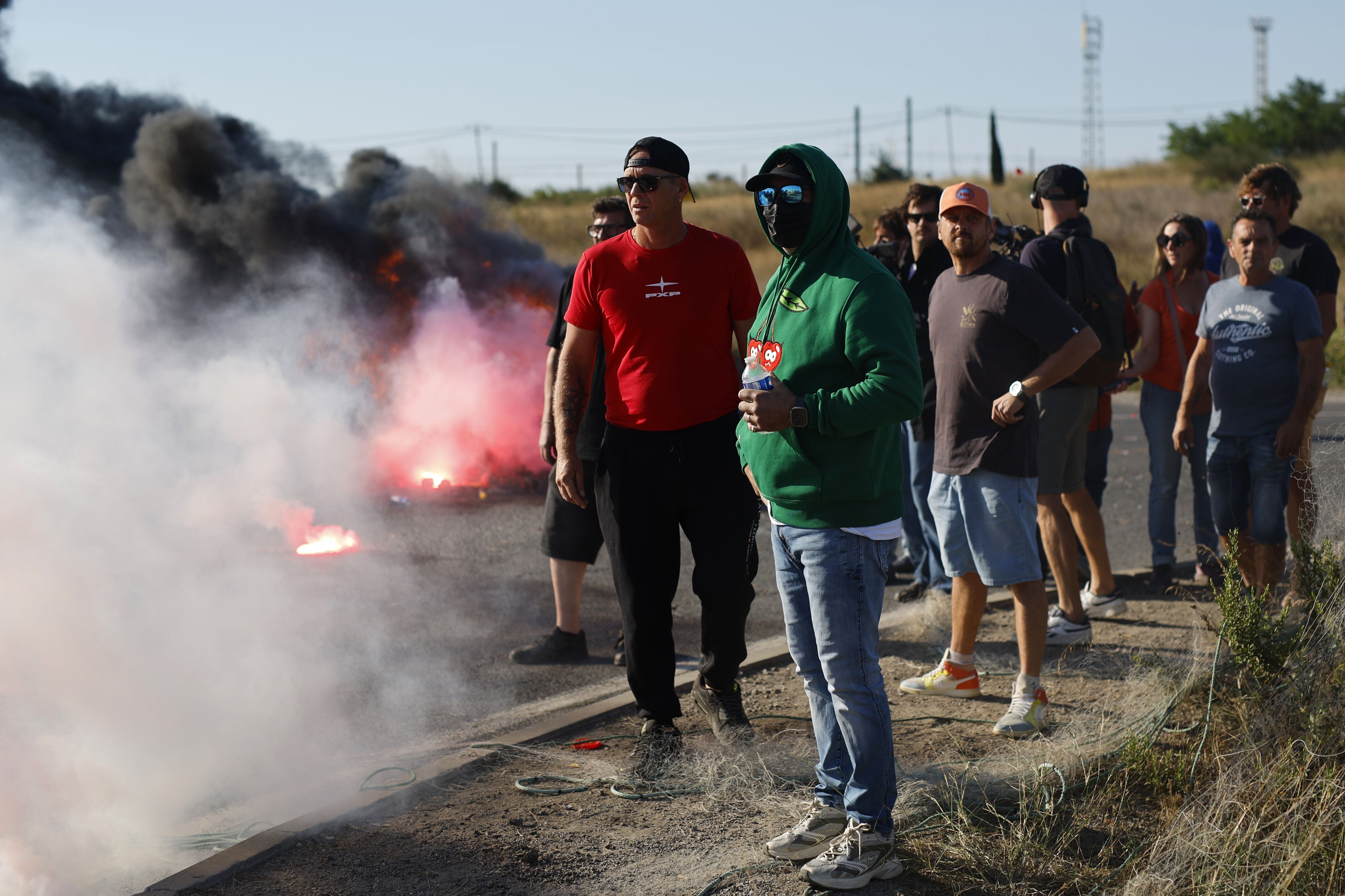 Mehrere Menschen stehen bei einer Straßenblockade mit brennenden Reifen und starkem Rauch.