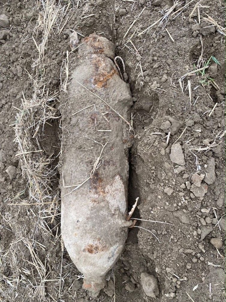 Eine alte, rostige Bombe liegt teilweise eingegraben im Erdreich.