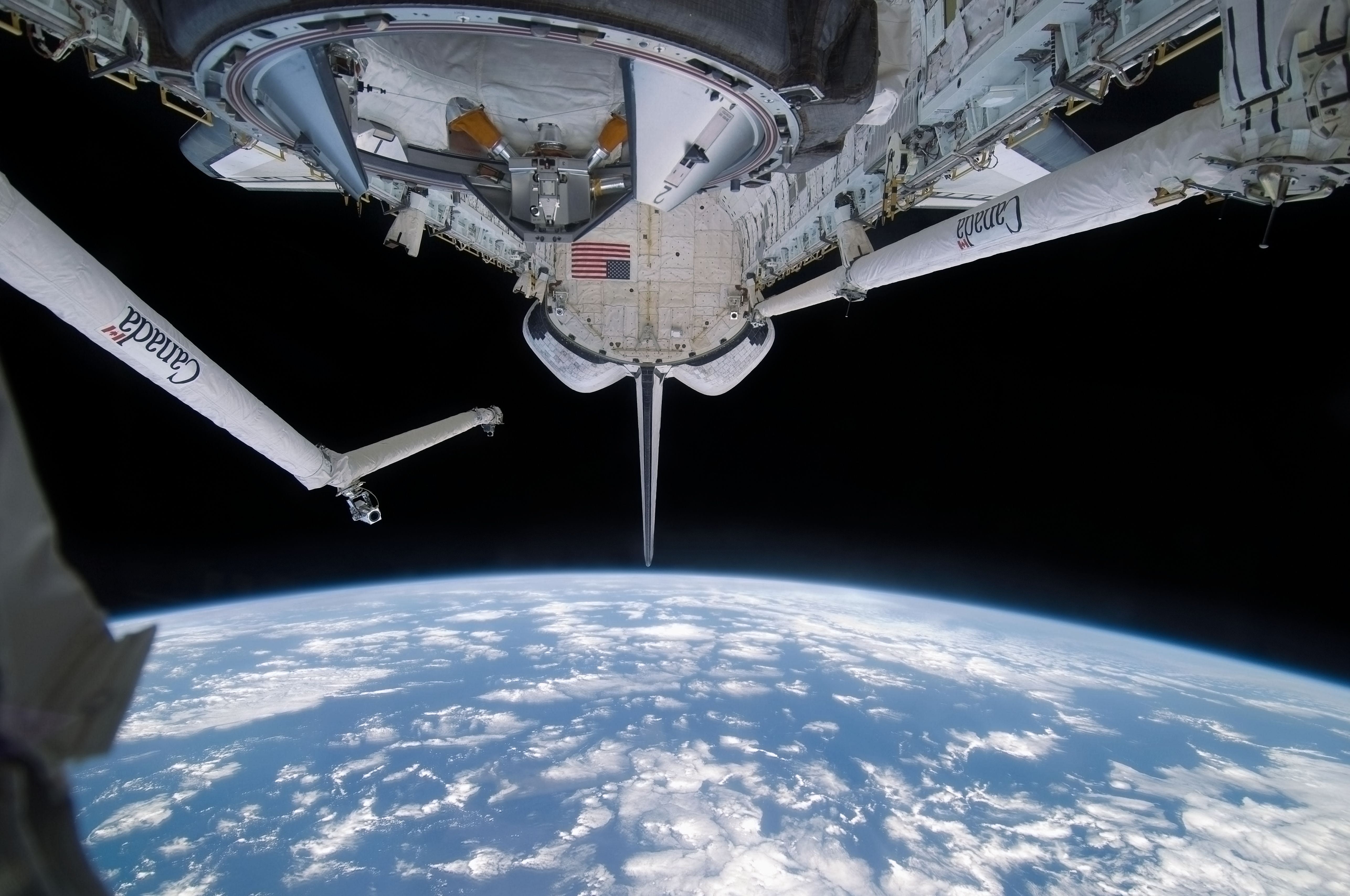 Das Space Shuttle Discovery über der Erde im All mit offener Nutzlastbucht und Roboterausleger.