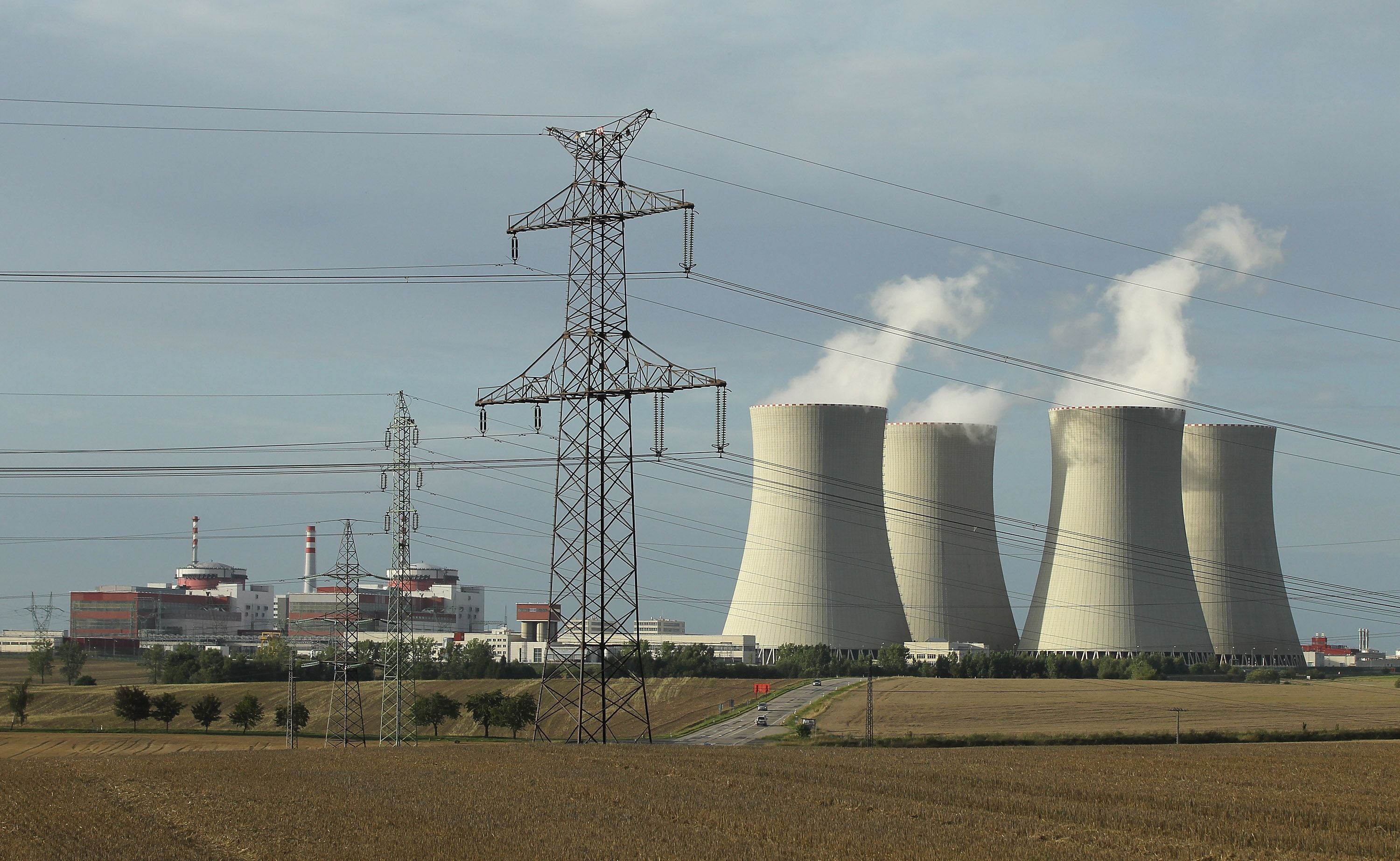 Ein Strommast steht vor vier Kühltürmen und zwei Reaktorblöcken eines Kernkraftwerks.
