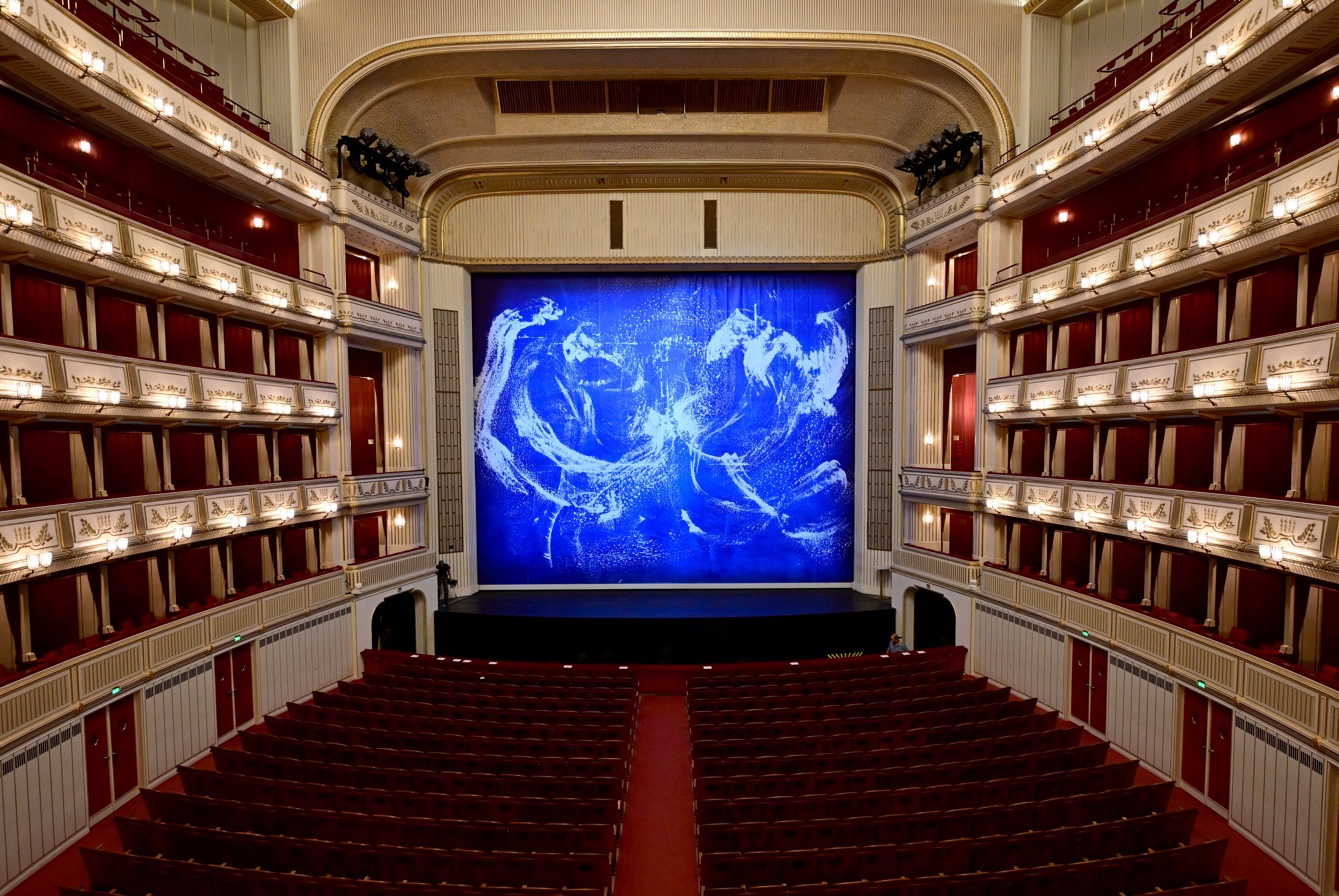 Blick in den Zuschauerraum der Wiener Staatsoper mit blauem Eisernen Vorhang auf der Bühne.