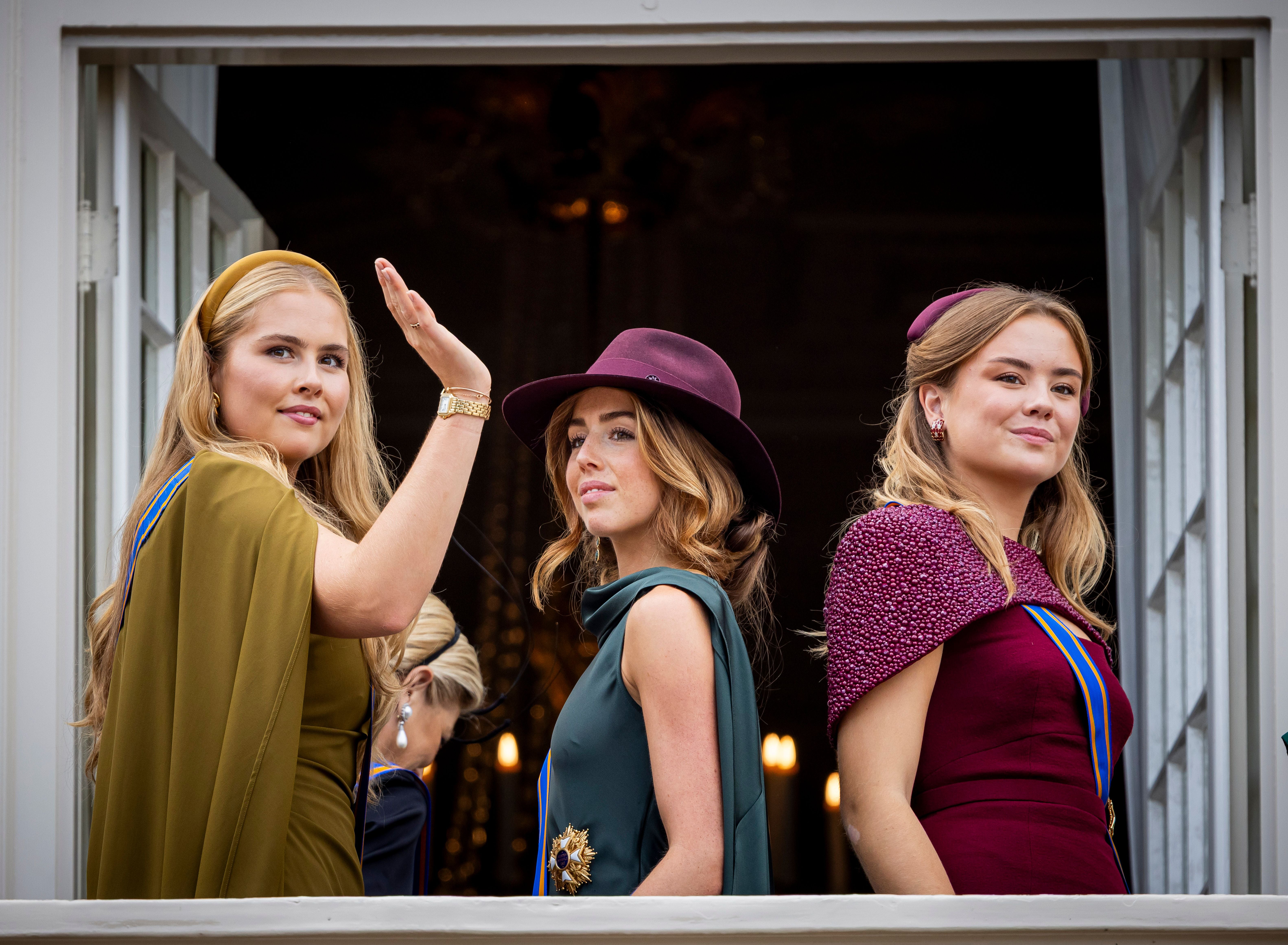 Drei junge Frauen in festlicher Kleidung stehen an einem offenen Fenster und blicken hinaus.
