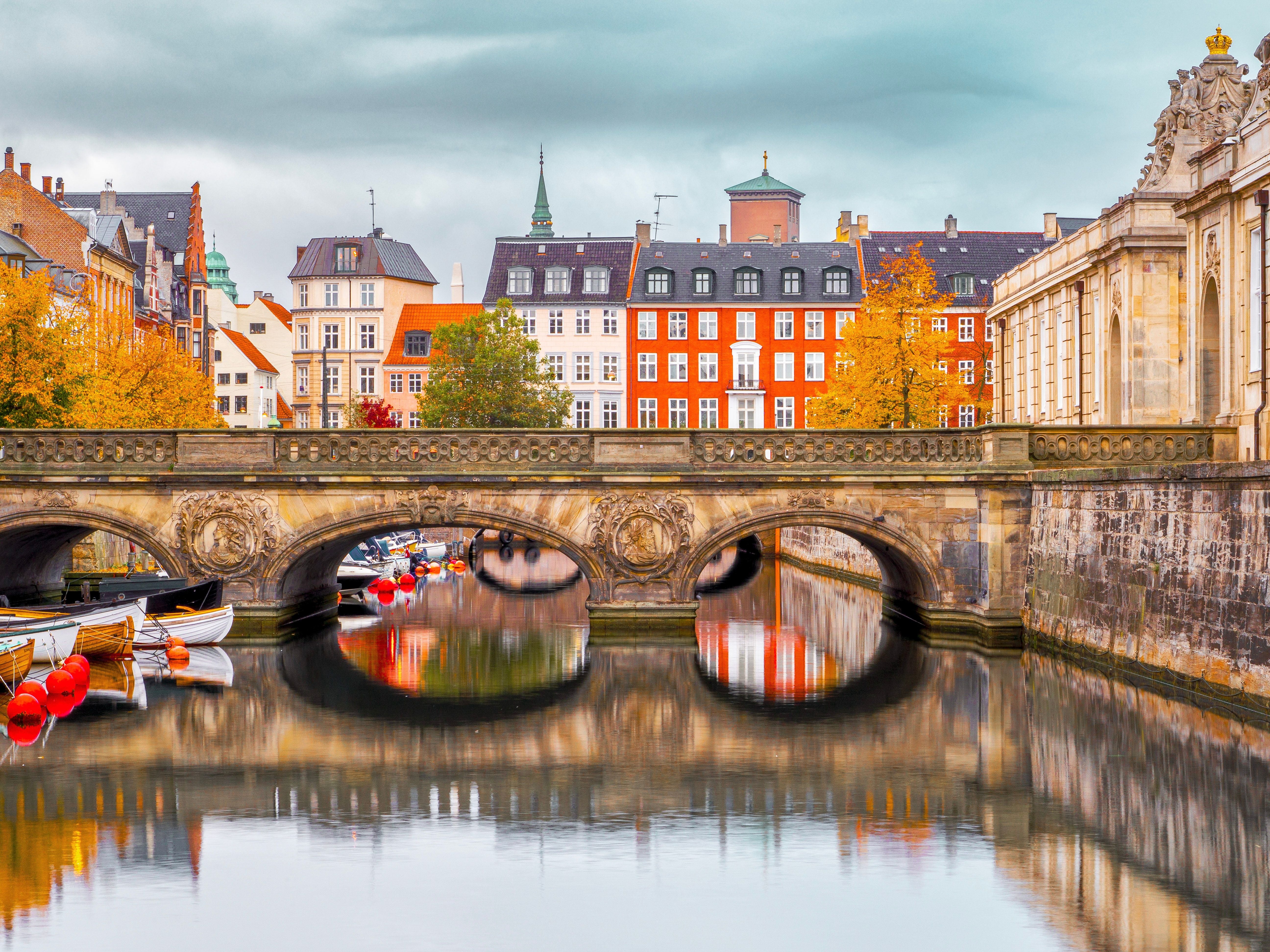 Herbstliche Szene mit dem Marmorbogen in Kopenhagen, reflektiert im ruhigen Wasser, bunte Häuser im Hintergrund.