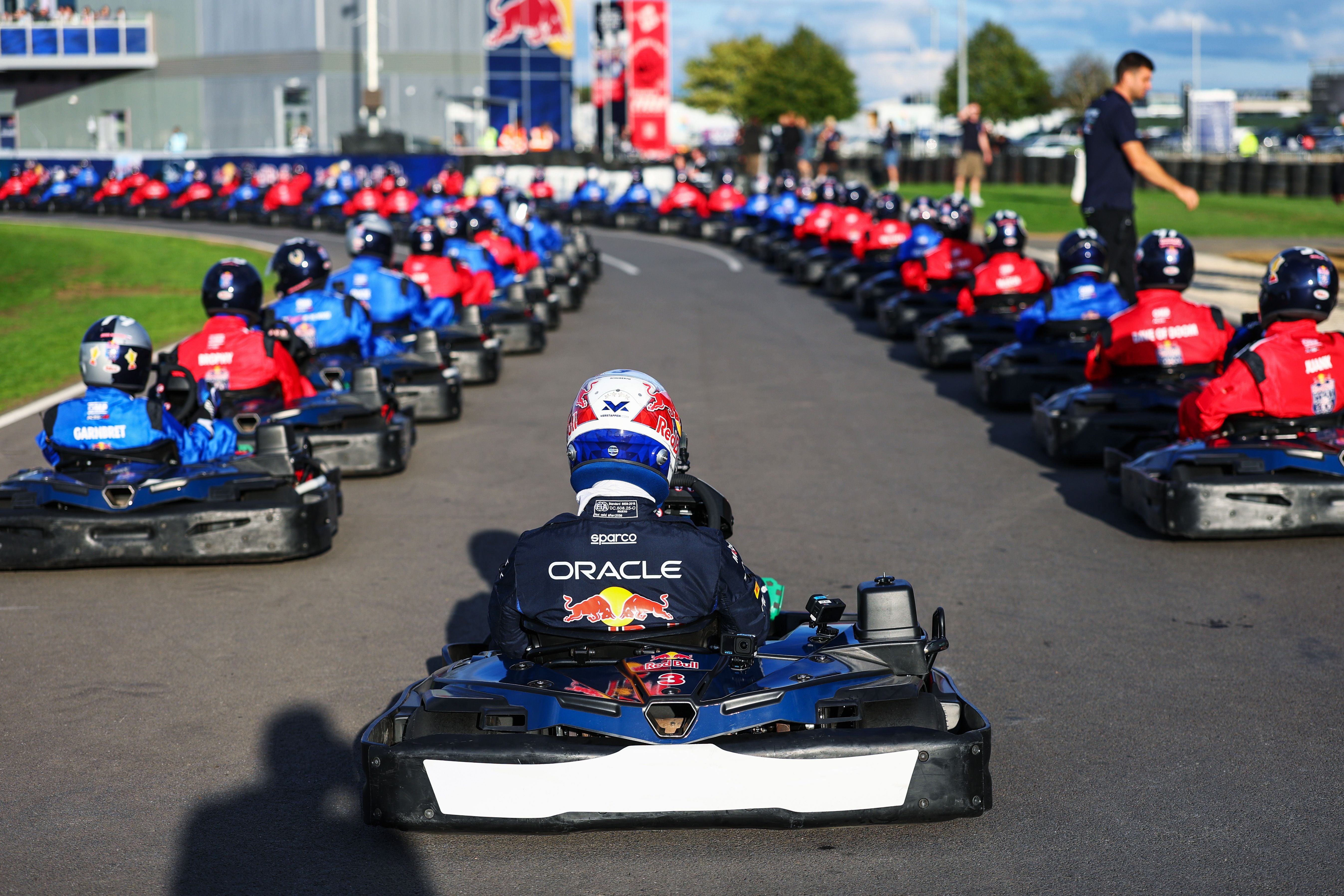 Viele Gokarts mit Fahrern in roten und blauen Overalls stehen startbereit auf einer Rennstrecke.