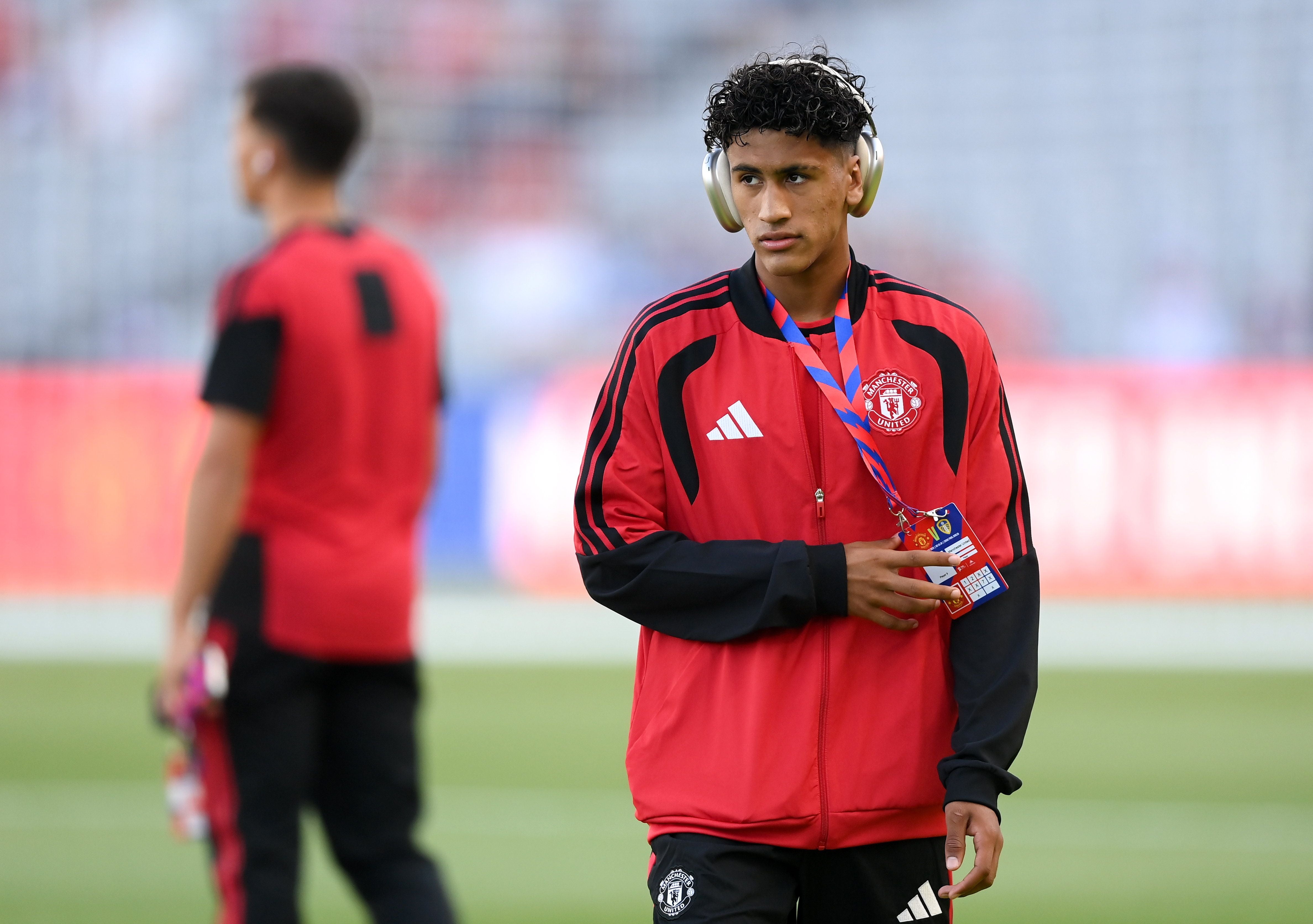 Ein junger Fußballer von Manchester United trägt Kopfhörer und einen Ausweis auf dem Spielfeld.