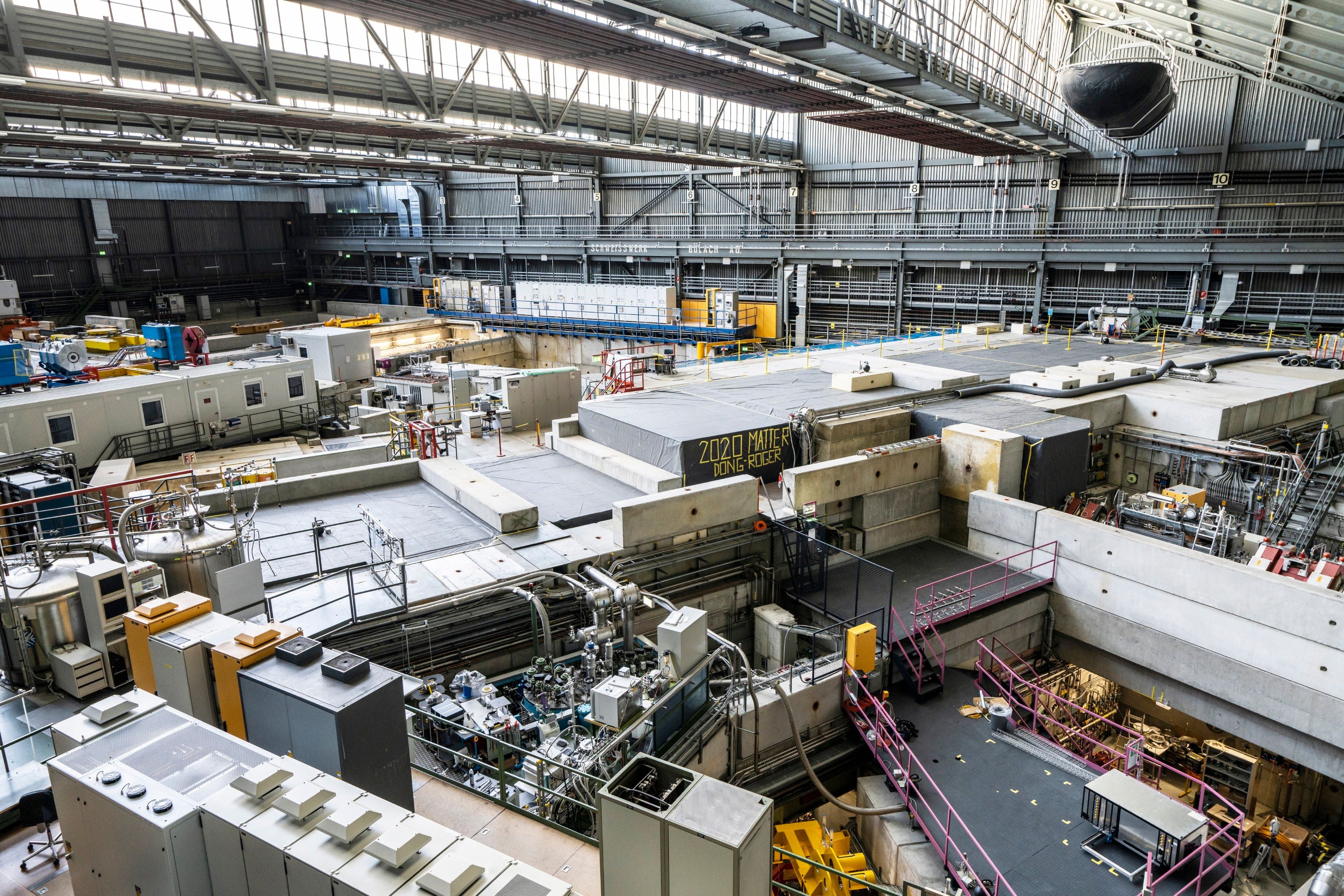 Blick in eine große Experimentierhalle mit Anlagen, Betonblöcken und technischen Geräten.
