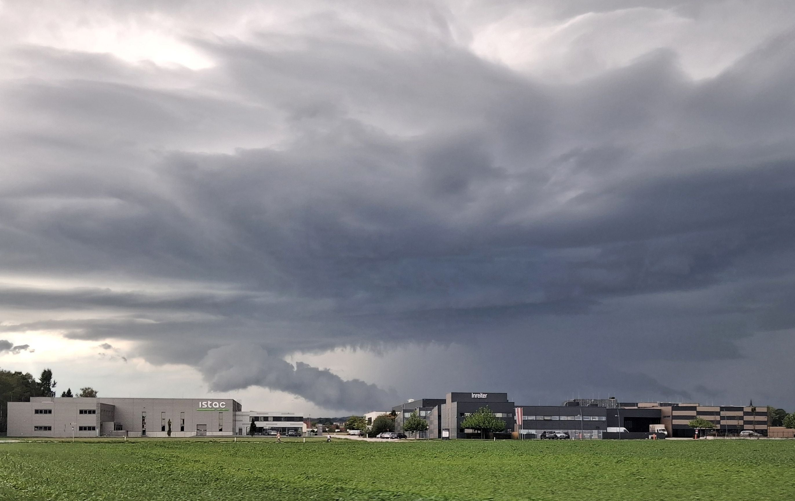 Dunkle Sturmwolken über Industriegebäuden und einem Feld in Pasching, Oberösterreich.