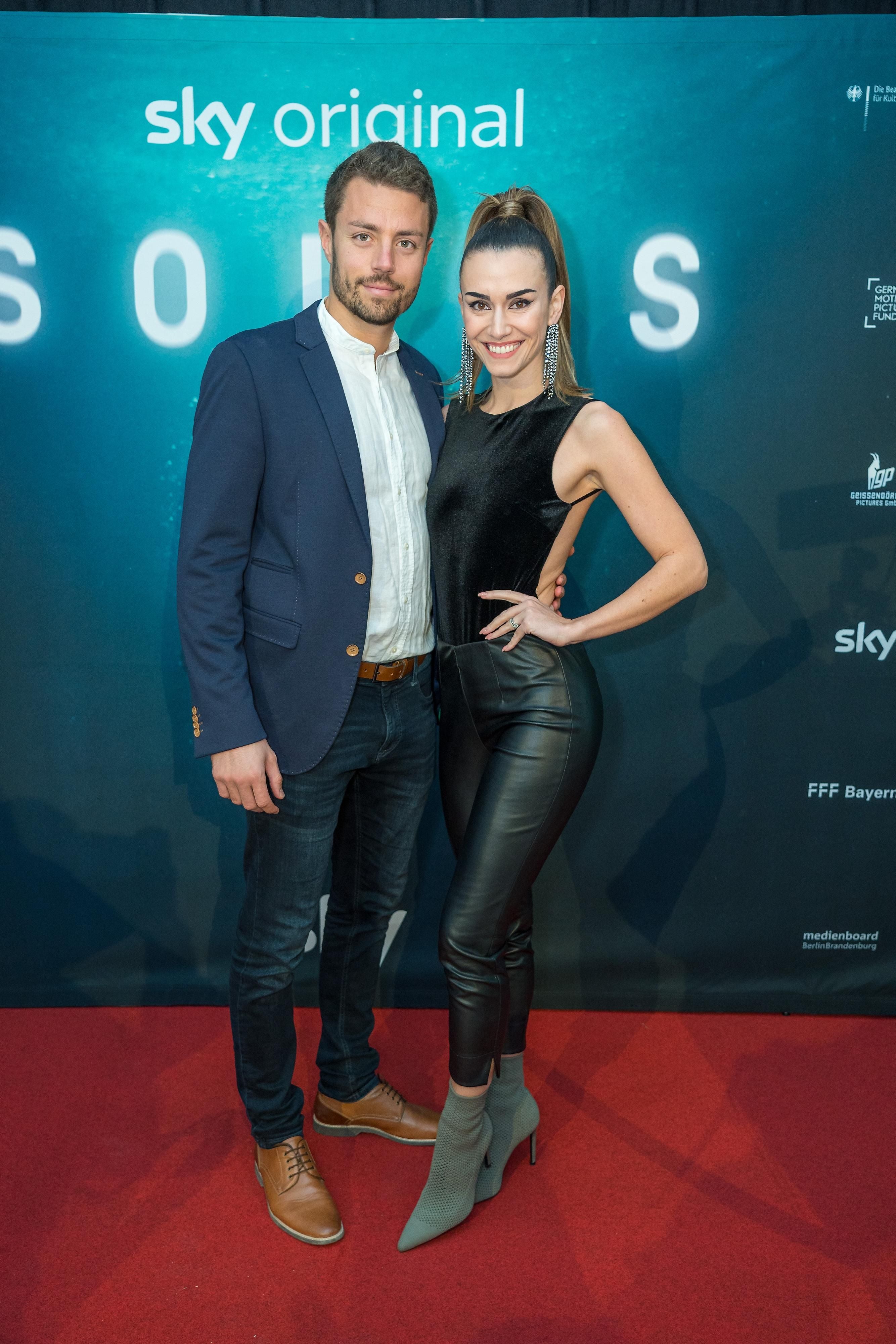 Ein Mann und eine Frau posieren auf dem roten Teppich vor einem "Sky Original"-Banner.