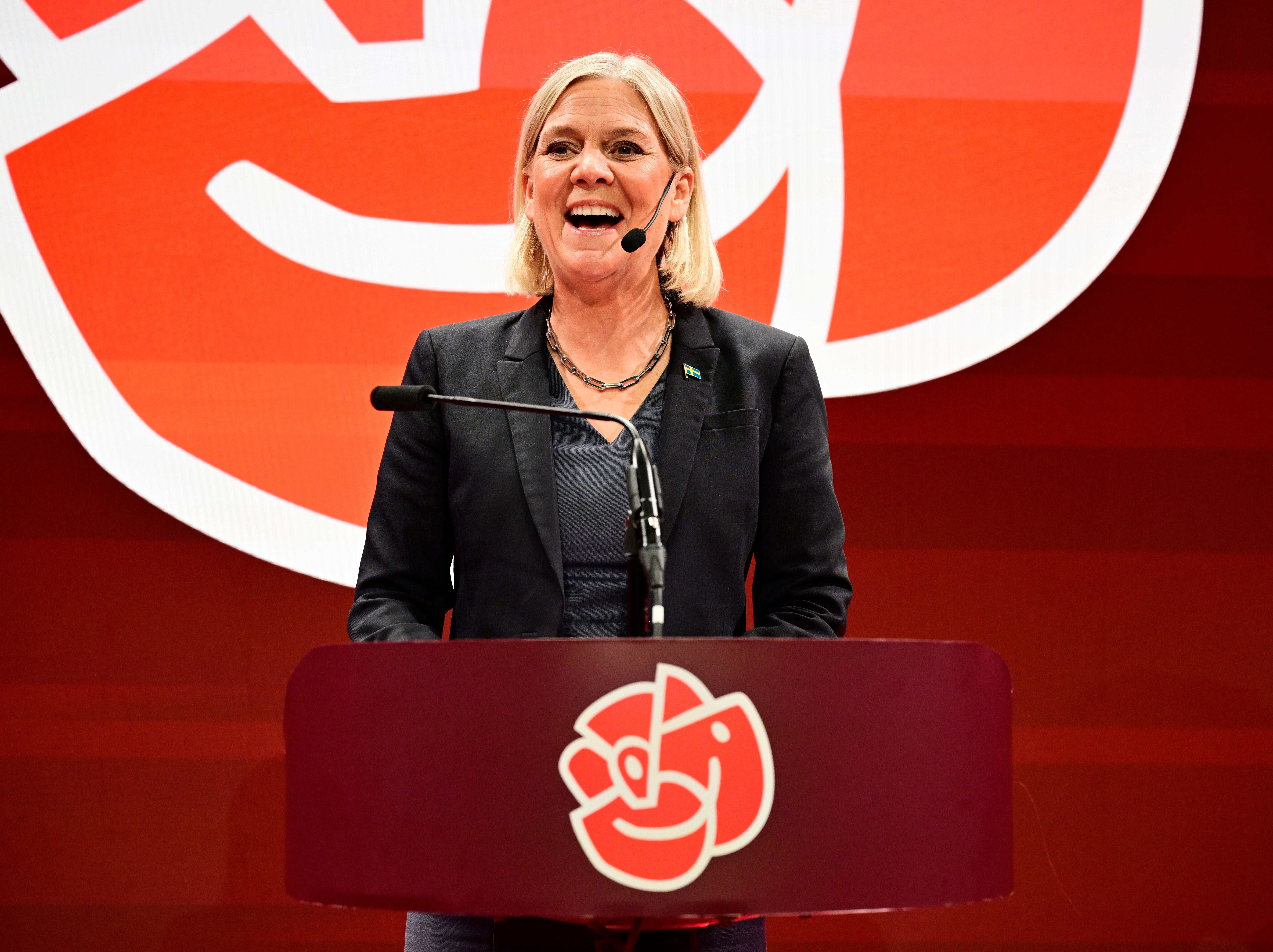 Eine Frau spricht lächelnd an einem Rednerpult mit sozialdemokratischem Symbol im Hintergrund.