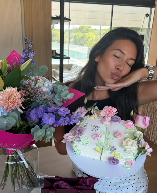 Frau posiert lächelnd mit Blumenstrauß und verzierter Geburtstagstorte zum 32. Geburtstag.