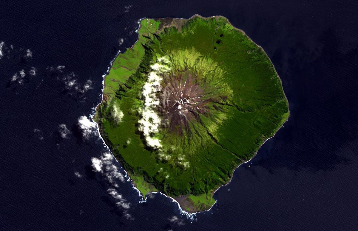 Satellitenbild einer grünen, runden Insel mit zentralem Vulkan, umgeben vom Meer.